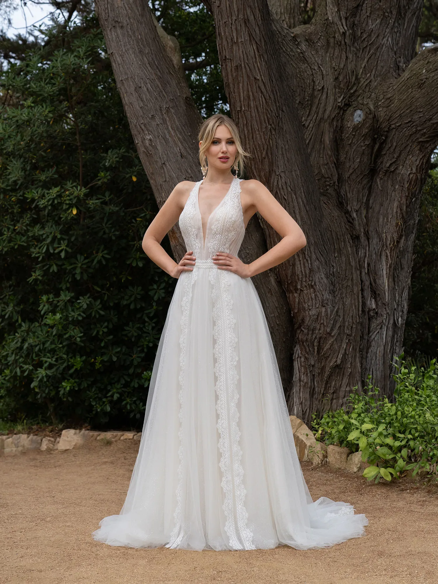 Braut im Hochzeitskleid mit Hände in den Hüften im Wald stehend