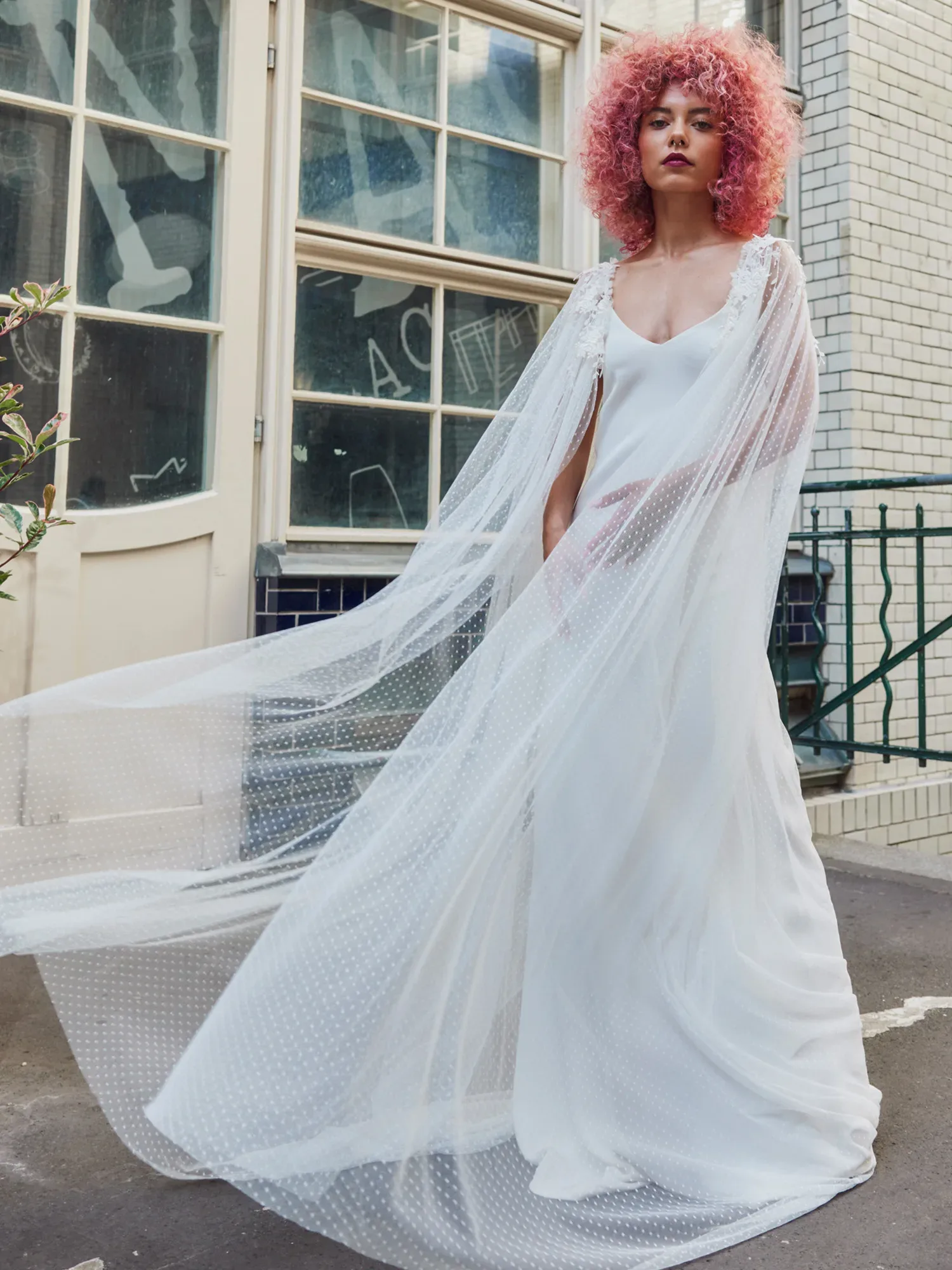 Braut im Hochzeitskleid mit rot gefärbten Haaren posiert auf einer Straße