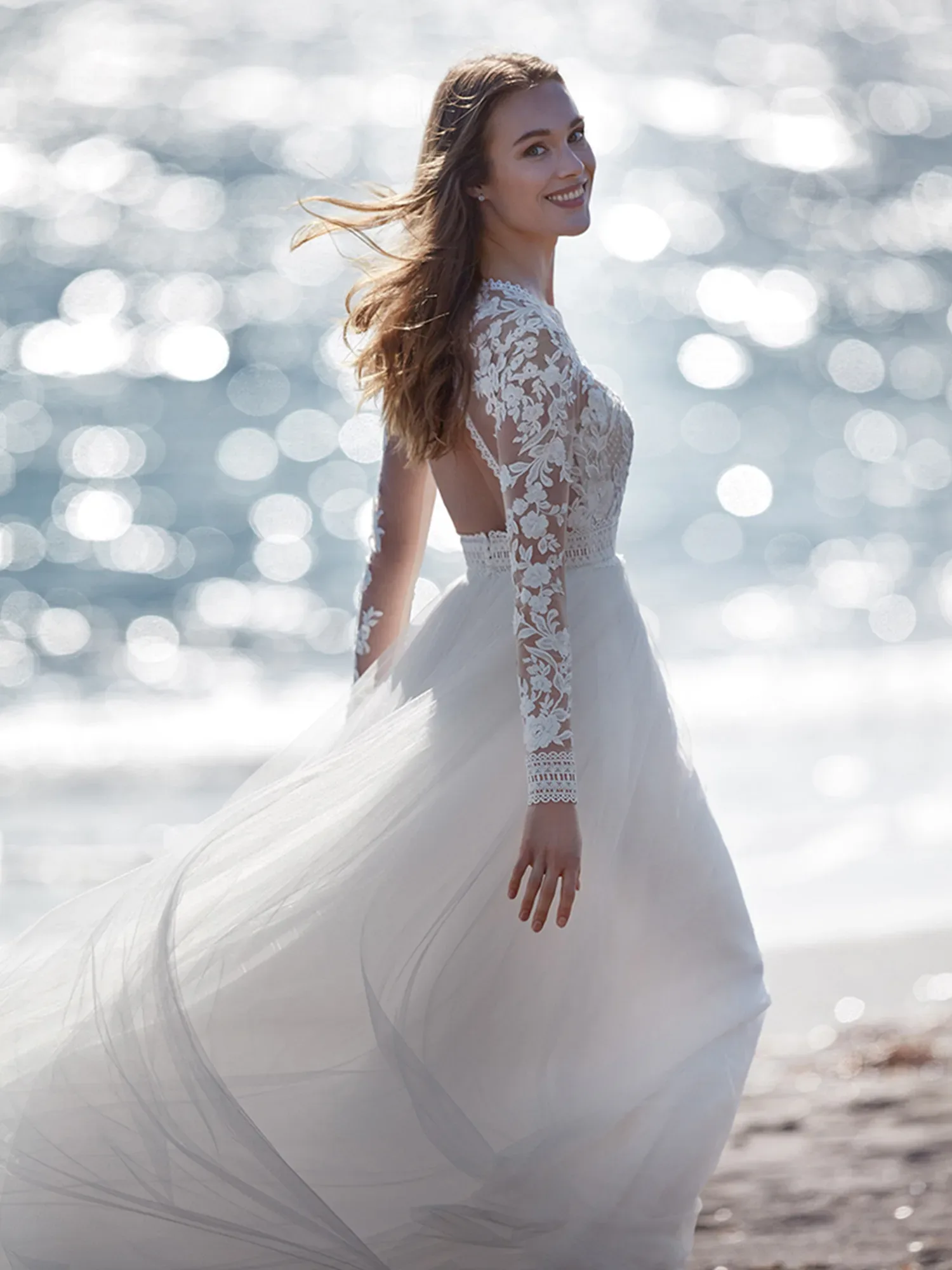 Braut im Hochzeitskleid mit Spitzenärmel am Strand entlang laufend