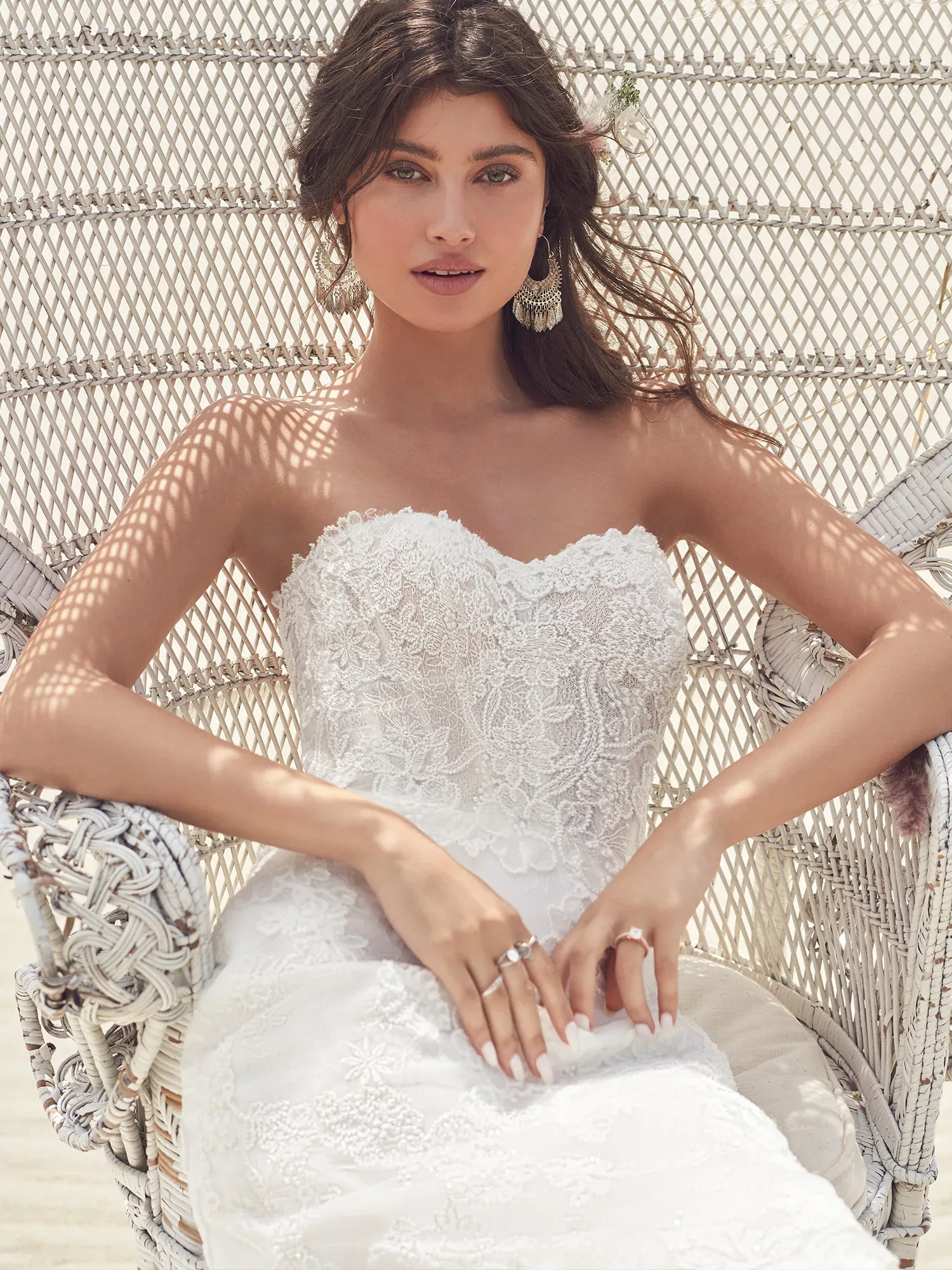 Braut in Hochzeitskleid aus Spitze am Strand in einem Stuhl sitzend