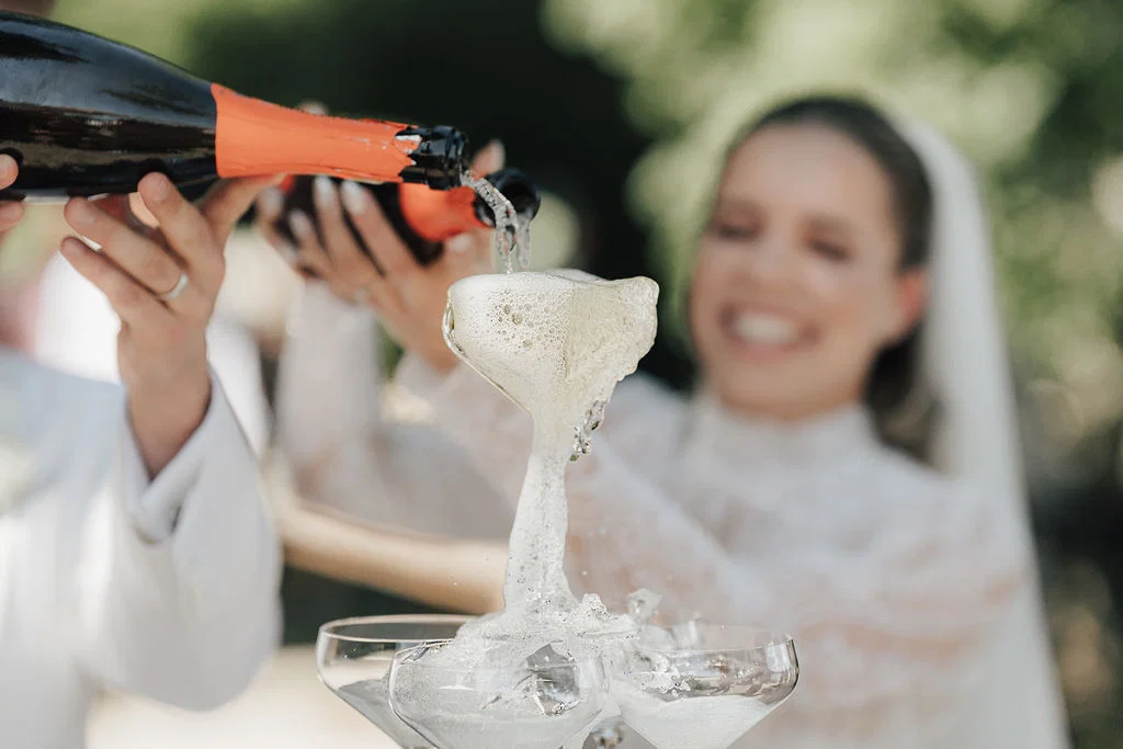 Braut und Bräutigam gießen Champagner in eine Glaspyramide, während der Schaum elegant über die Gläser fließt.