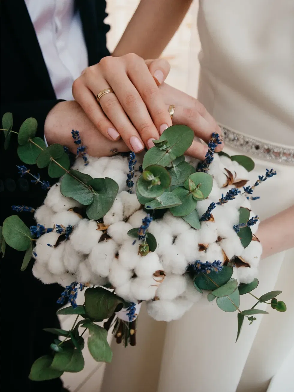 Ein romantisches Bild eines Brautpaares mit zarten Eheringen, die über einem Strauß aus Baumwolle, Eukalyptus und Lavendel ruhen.