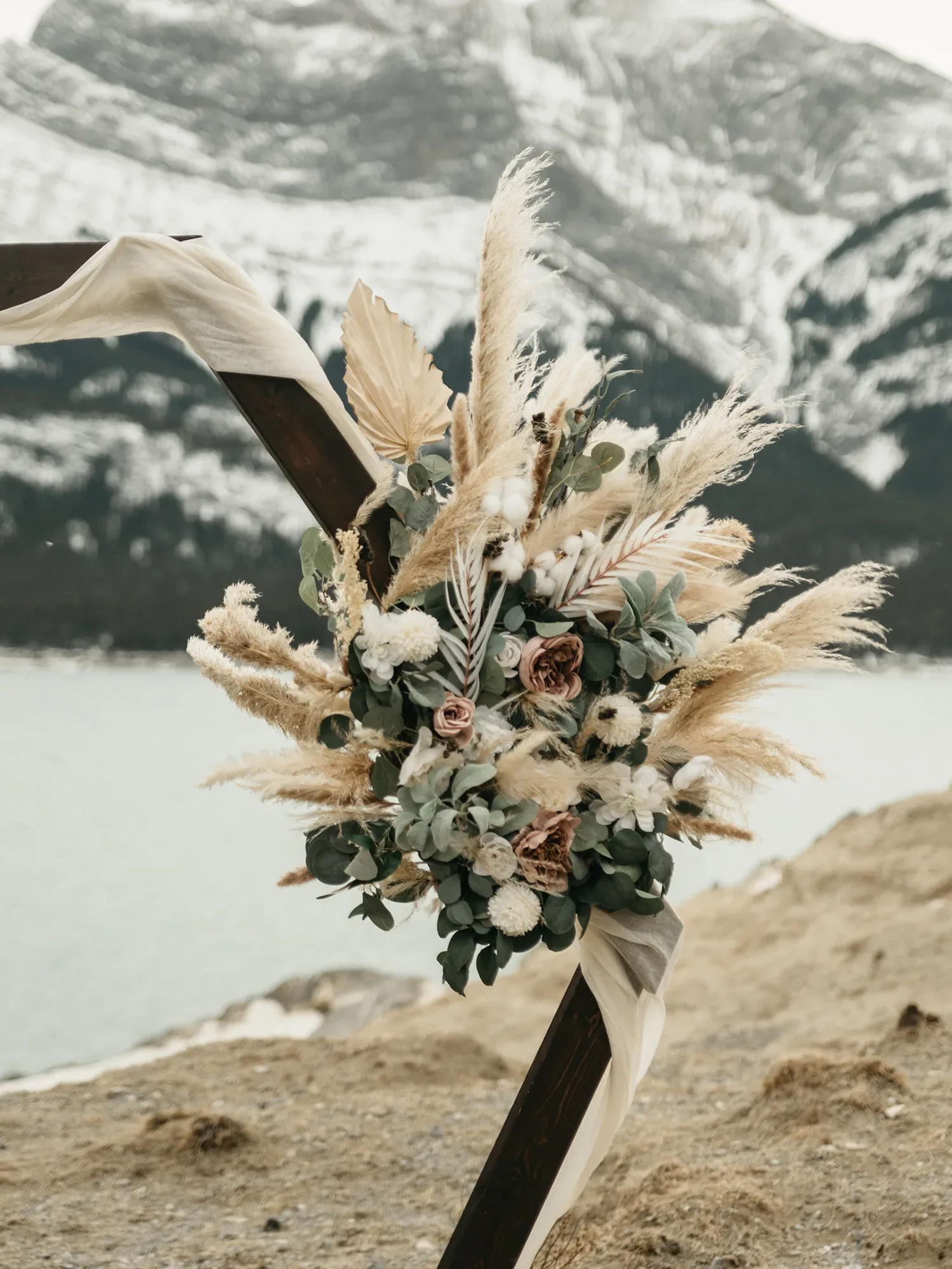 Ein Boho-inspirierter Blumenstrauß mit Pampasgras, Eukalyptus und Trockenblumen, der vor einer malerischen Berglandschaft arrangiert ist.