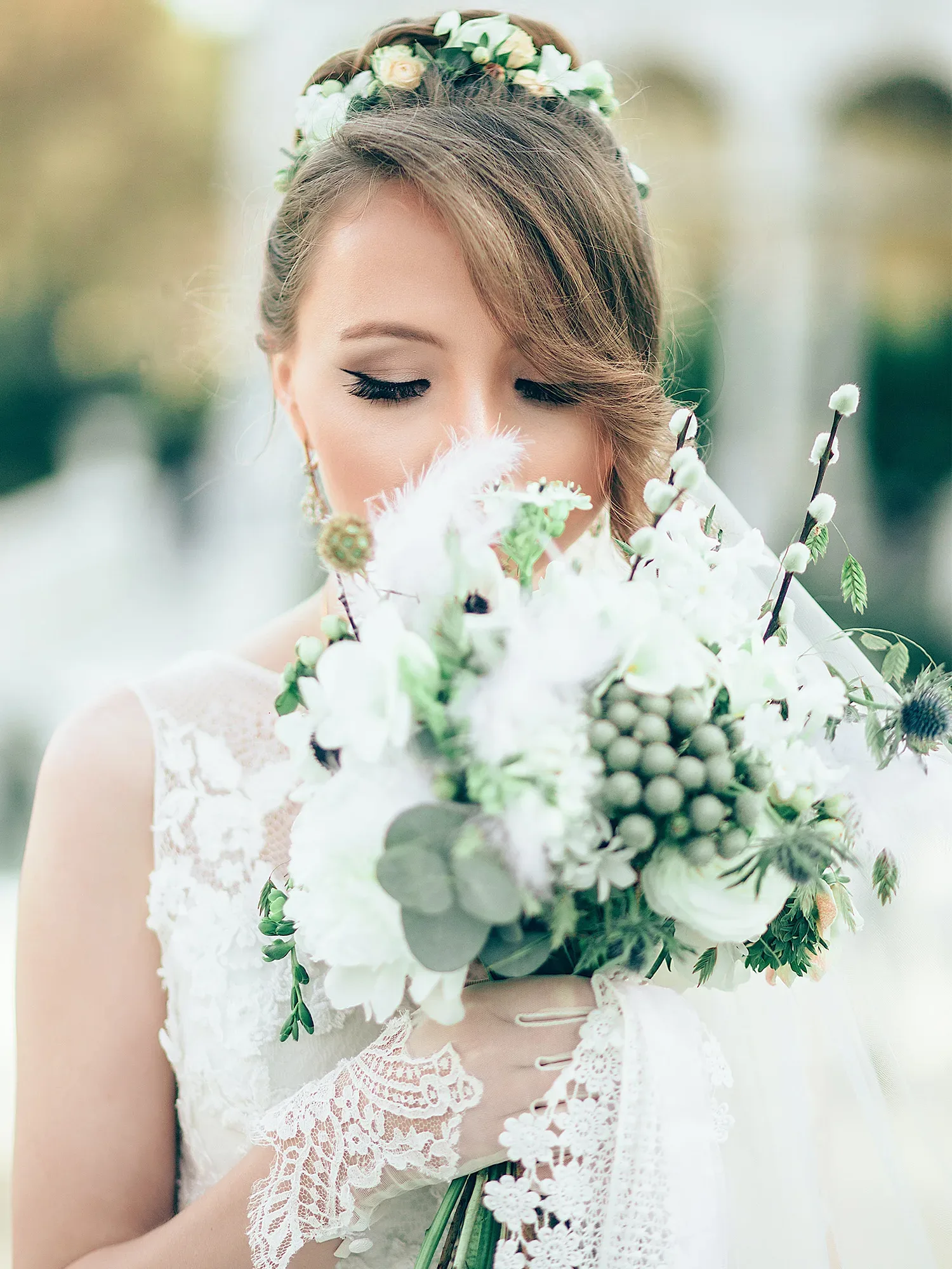 Die Braut hält ihren opulenten Hochzeitsstrauß mit weißen Blumen und zarten Federn, während sie zärtlich die Augen schließt.