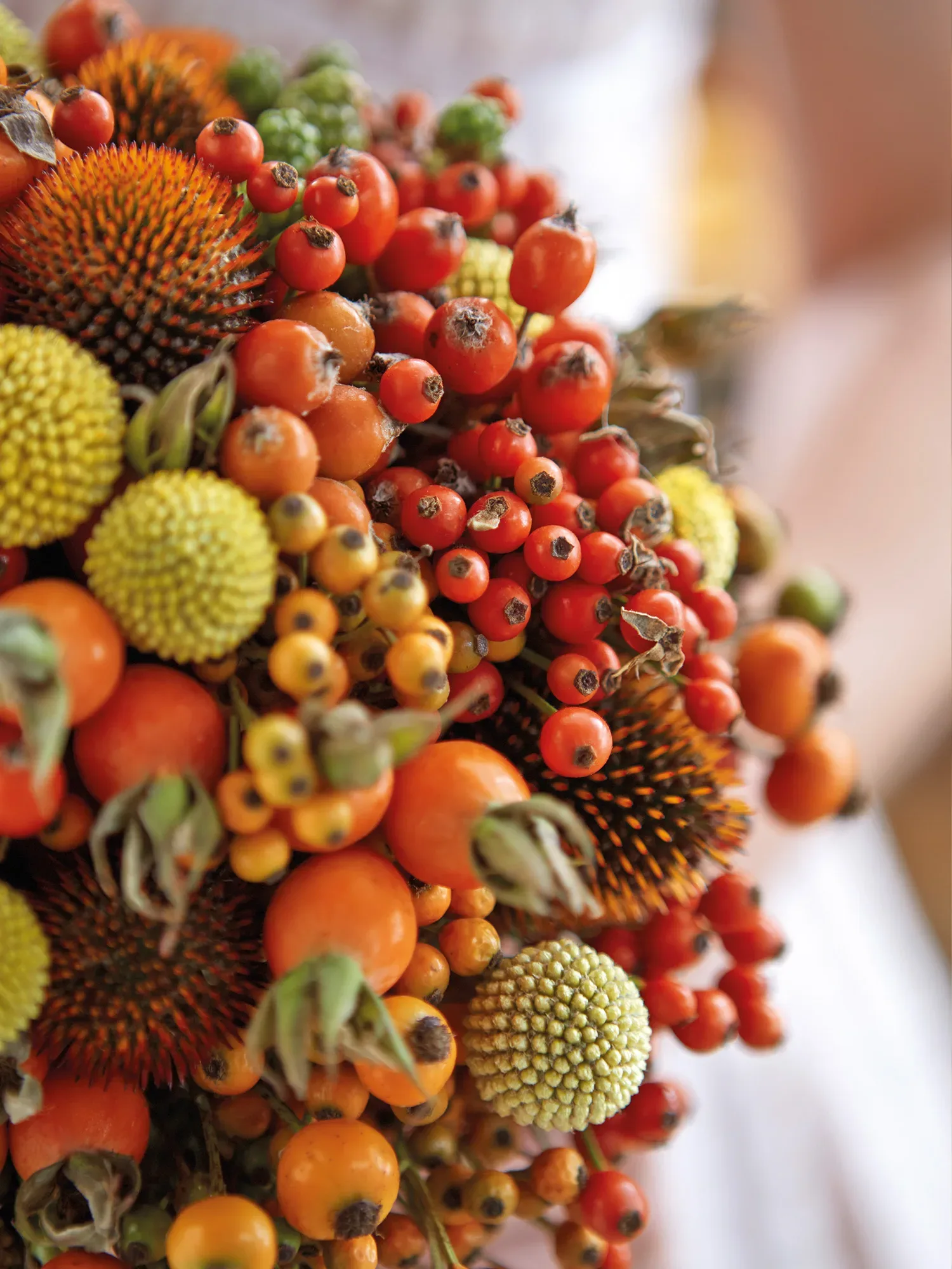 Nahaufnahme eines bunten Brautstraußes mit leuchtenden Beeren und Früchten in warmen Orange- und Gelbtönen, ideal für eine Herbsthochzeit.