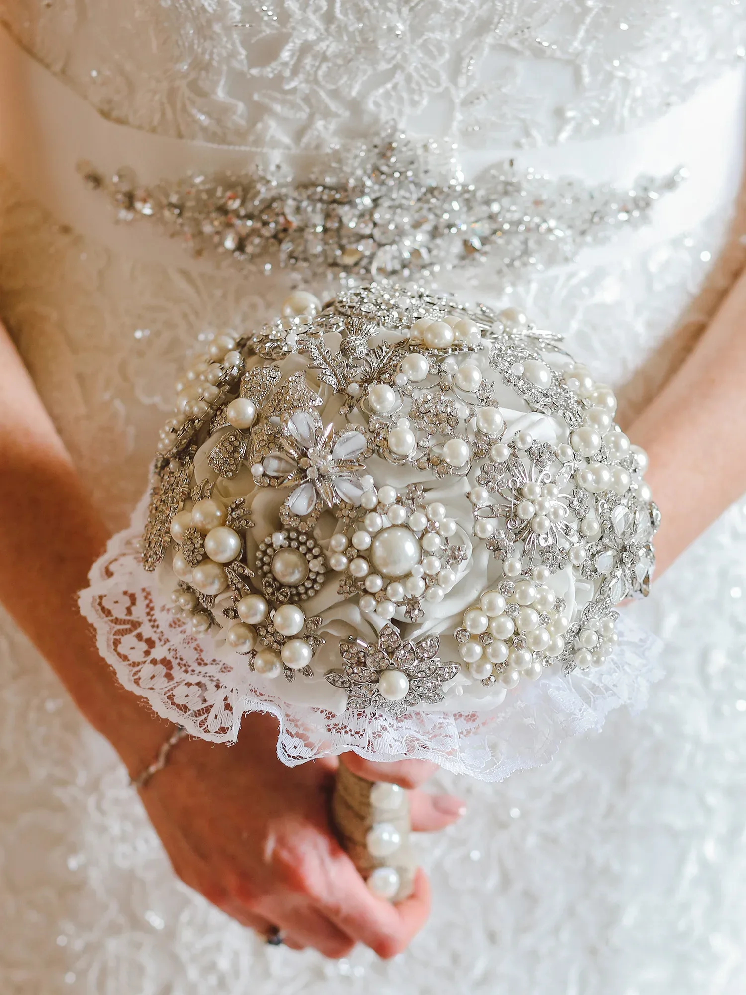 Eine Braut hält einen kunstvoll gefertigten Strauß aus Perlen und glitzernden Schmuckelementen, passend zum eleganten Brautkleid.
