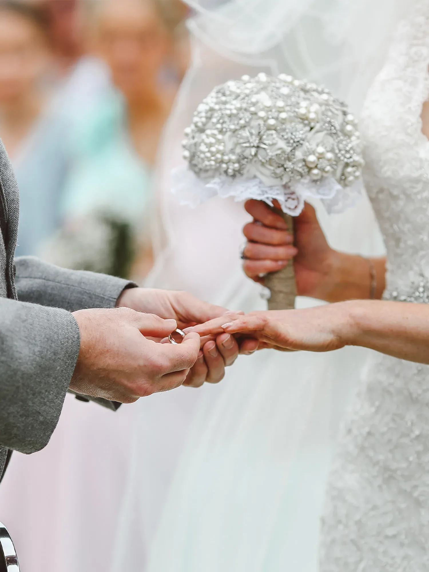 Die Braut und der Bräutigam tauschen Ringe während der Trauung, die Braut hält dabei einen luxuriösen Strauß aus Perlen und Strass.