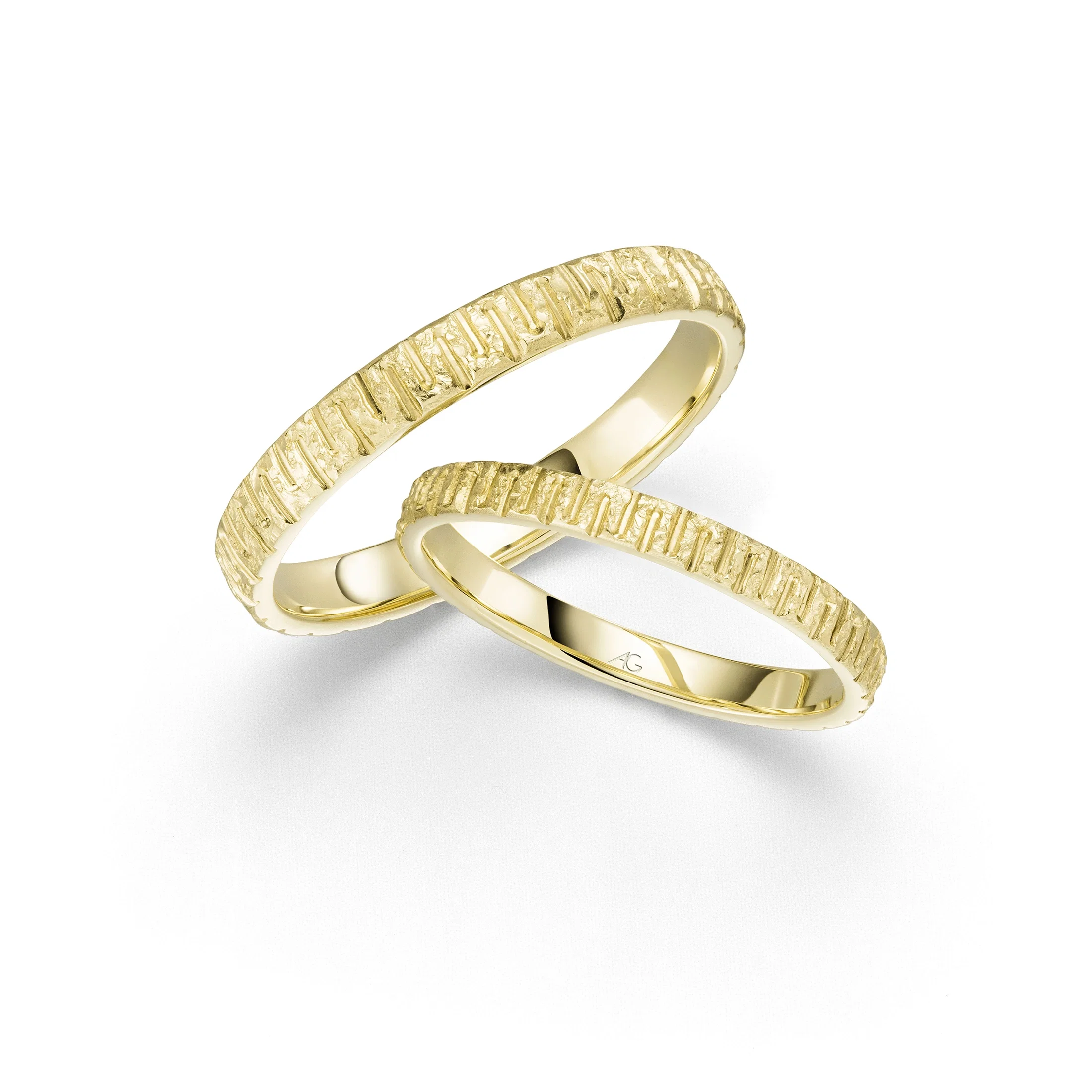 Zwei ineinanderliegende Trauringe aus Gelbgold mit strukturierter, leicht unregelmäßiger Oberfläche auf hellem Hintergrund