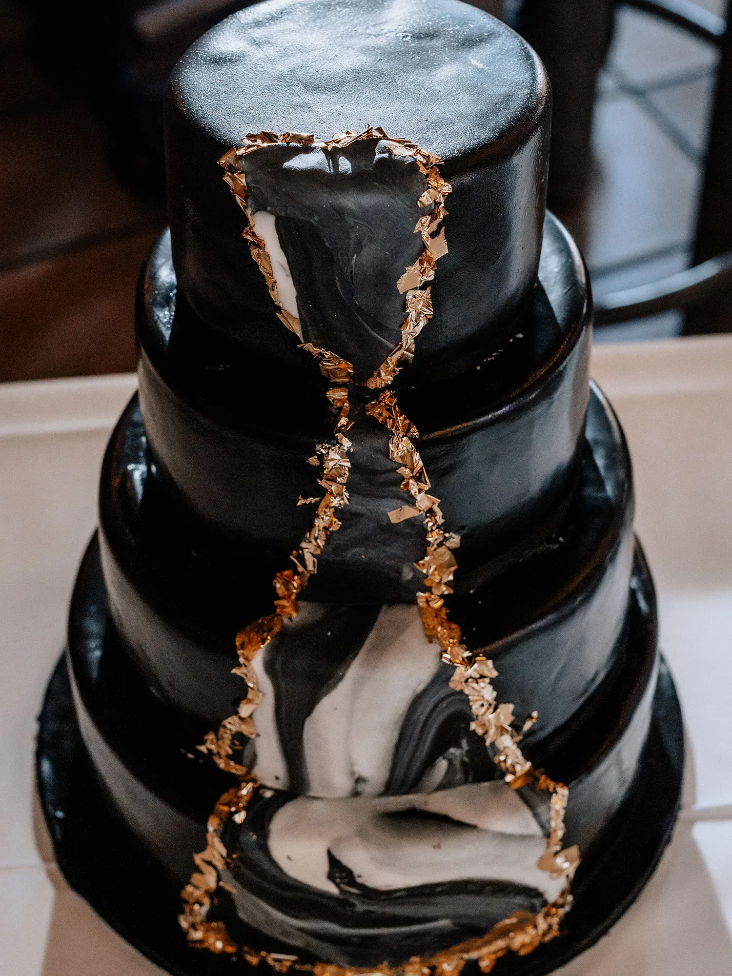 Moderne, mehrstöckige Hochzeitstorte in Schwarz mit goldenen Verzierungen und marmorierten Details. Die geometrischen Linien und die luxuriösen Goldelemente verleihen der Torte einen auffälligen und eleganten Look.