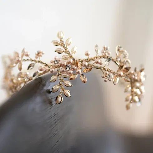 Detailaufnahme einer goldenen Tiara mit zarten Perlen und funkelnden Kristallen in floralem Design, ideal für eine romantische Hochzeitsfrisur.