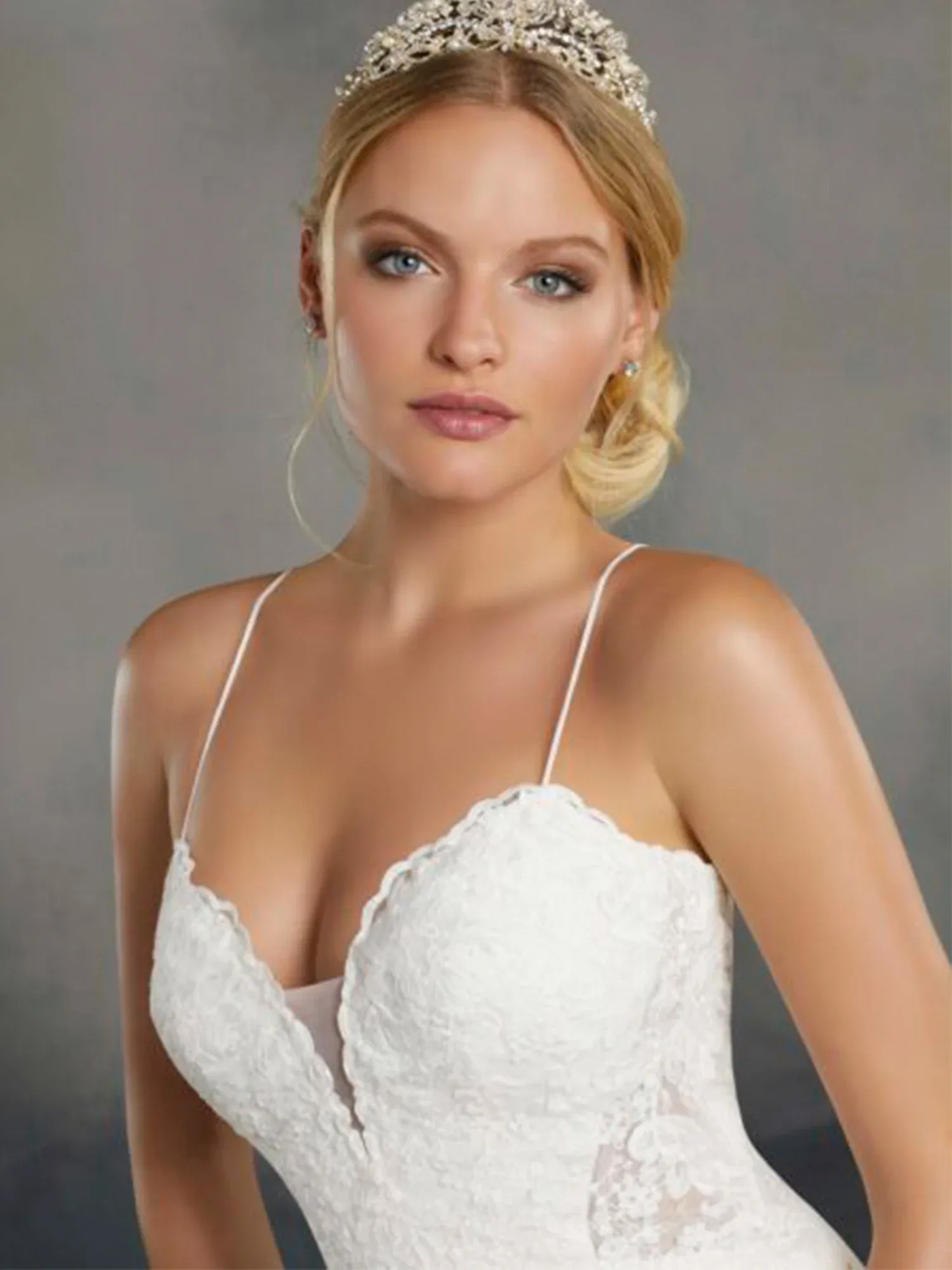 Eine Braut in einem weißen Spitzenkleid trägt eine funkelnde Tiara und hat ihre Haare elegant hochgesteckt. Ihr Make-up ist dezent gehalten.