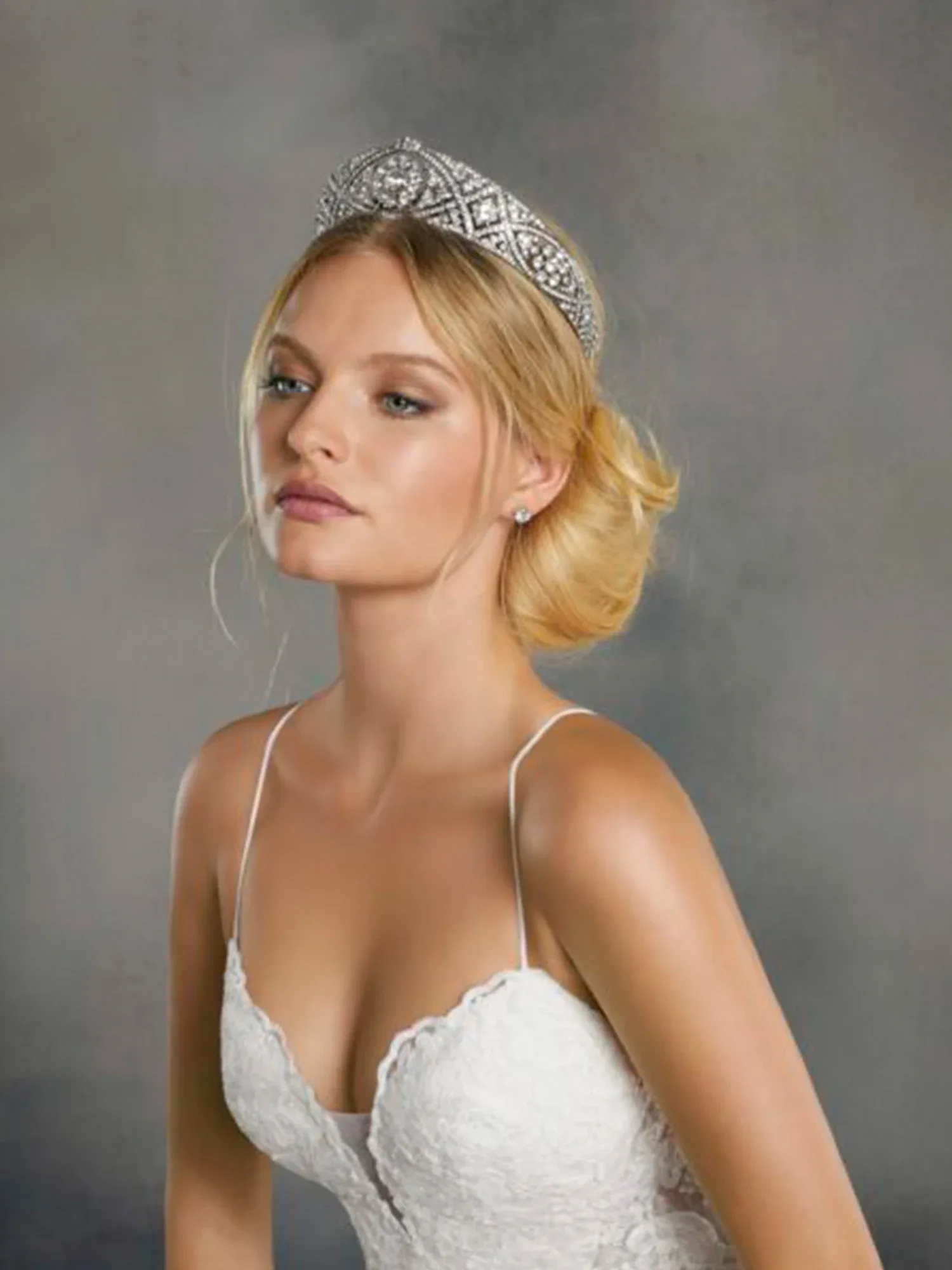 Eine Braut mit einem schlichten weißen Hochzeitskleid und einer eleganten, dezenten Tiara trägt ihr Haar in einer klassischen Hochsteckfrisur.