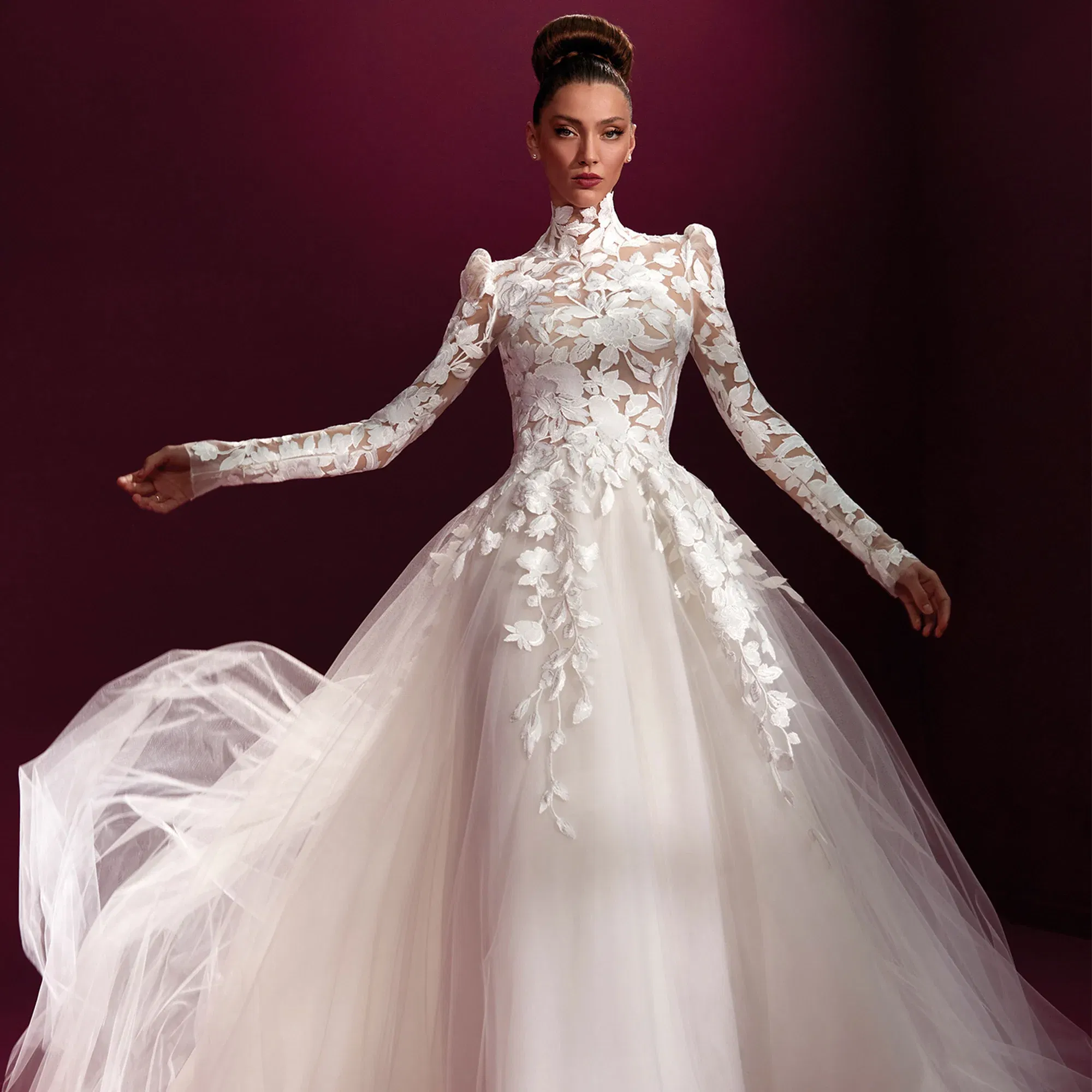 Brautkleid mit langen Spitzenärmeln und hochgeschlossenem Kragen, Vorderansicht. Der voluminöse Tüllrock und die floralen Applikationen auf dem Oberteil sorgen für einen klassischen, eleganten Look."