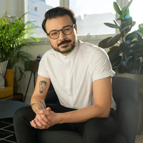 Porträt von Umut C. Özdemir, der in einem weißen Hemd in einem modernen Wohnzimmer sitzt und freundlich in die Kamera schaut.