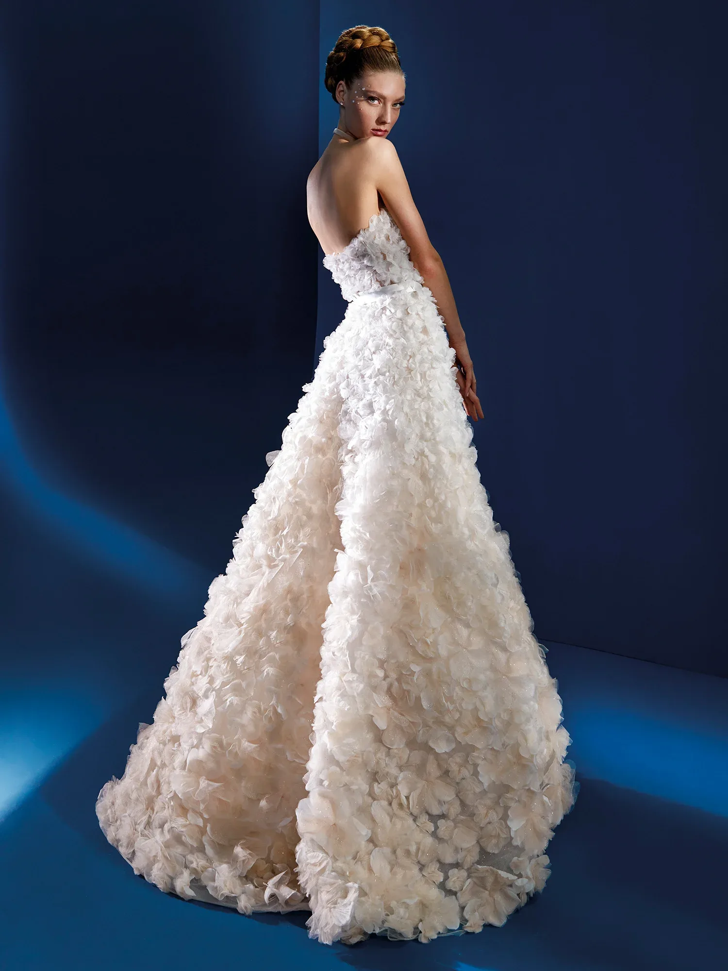 Rückenansicht eines trägerlosen Brautkleides mit voluminösem Rock, der mit großen, blütenartigen Applikationen verziert ist. Das strukturierte Design verleiht dem Kleid eine romantische und zugleich moderne Note.