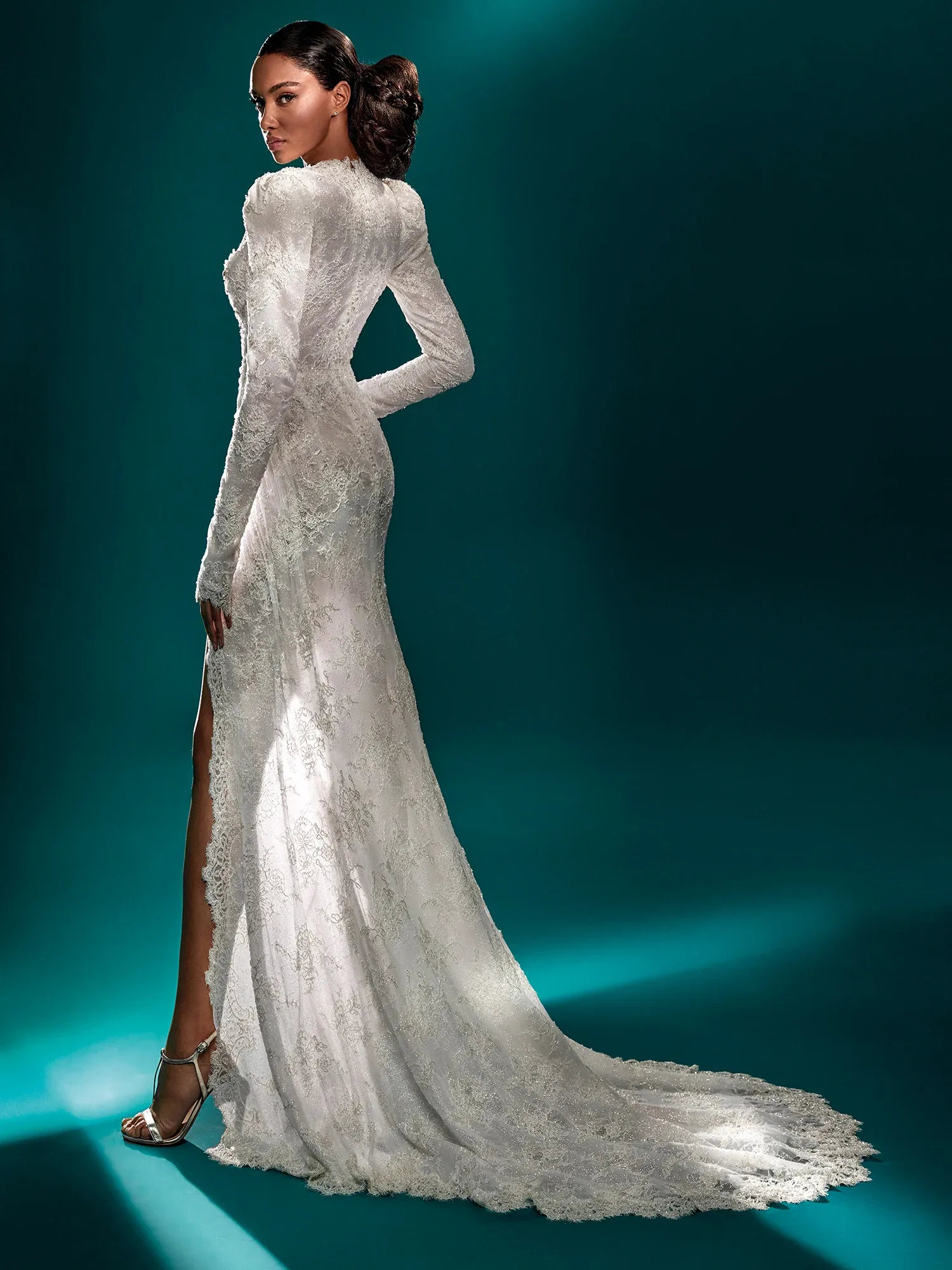 Rückenansicht eines figurbetonten Brautkleides mit langen Ärmeln und zarten Spitzenverzierungen. Das Kleid hat eine dezente Schleppe und einen hohen Beinschlitz, der dem eleganten Design eine moderne Note verleiht.