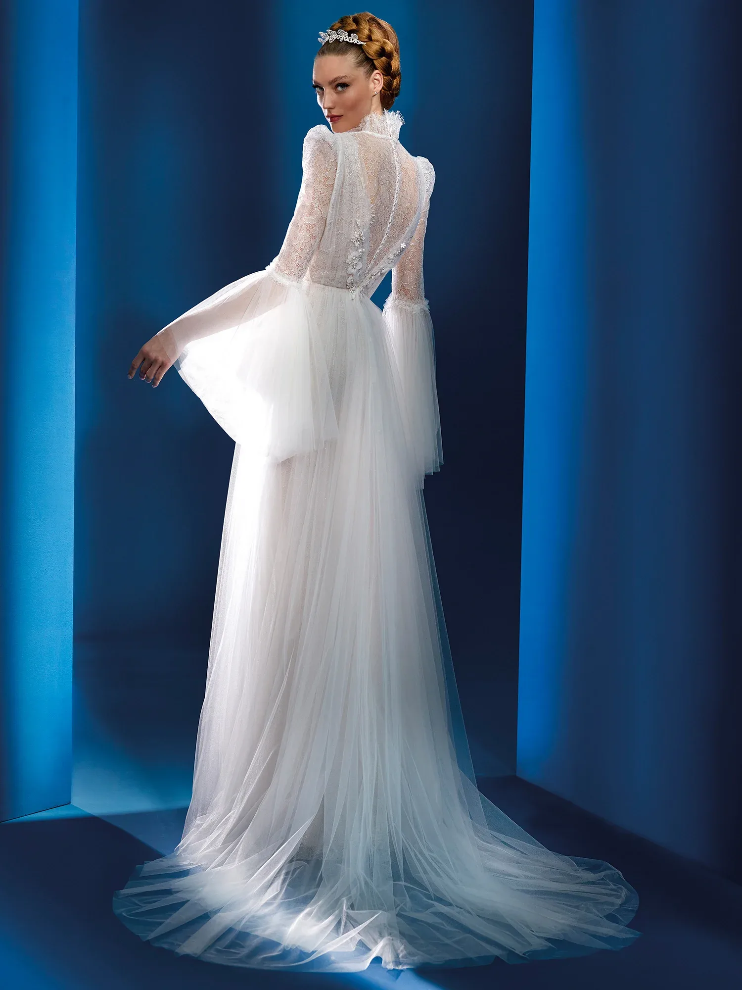 Rückenansicht eines romantischen Brautkleides mit langen Spitzenärmeln und transparentem Rückenteil. Das Kleid hat einen voluminösen, fließenden Tüllrock und betont durch den hohen Kragen sowie die verspielten Glockenärmel eine elegante Vintage-Ästhetik.