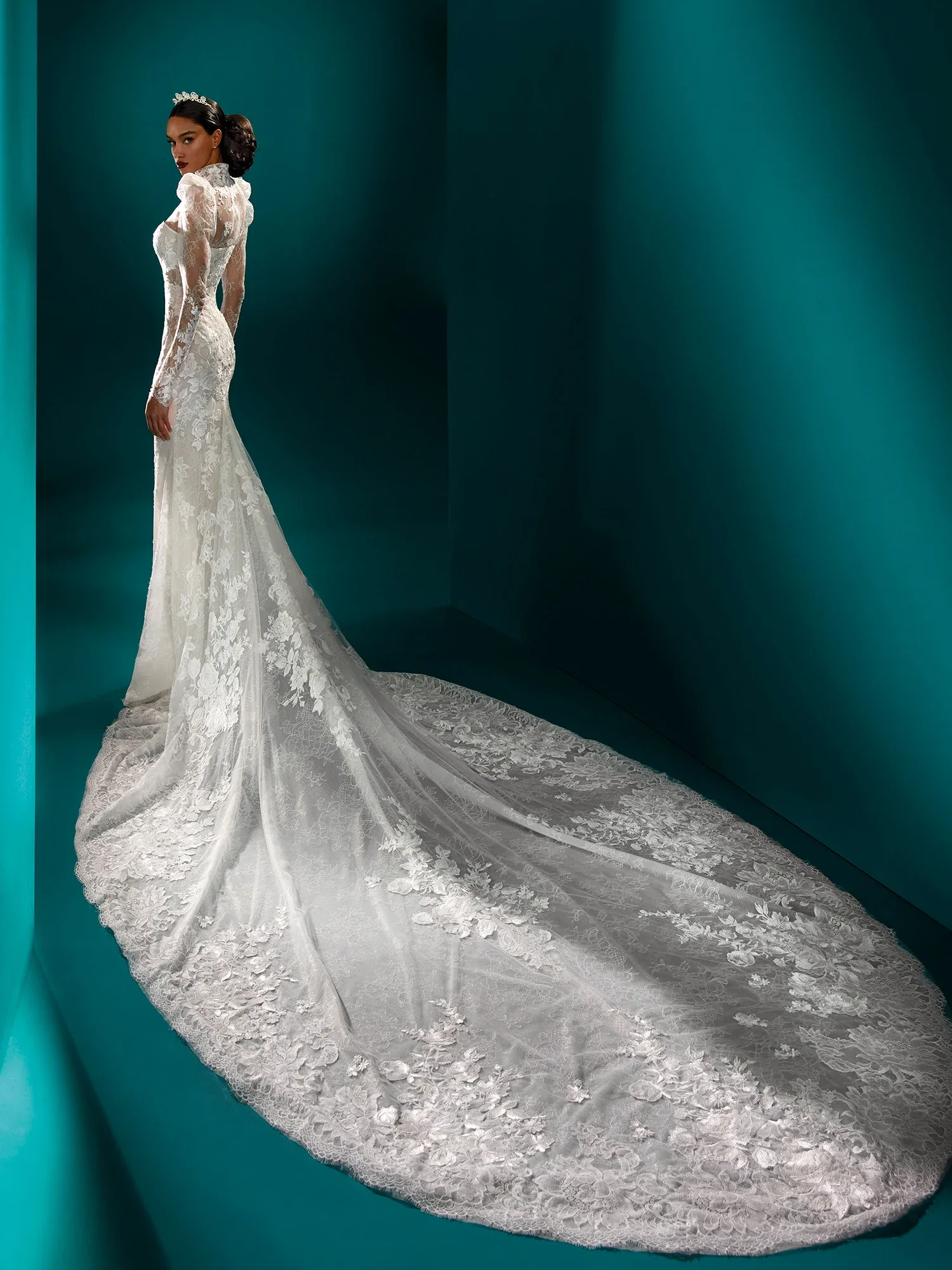 Rückenansicht eines eleganten Brautkleides mit langer Spitzenschleppe. Das Kleid hat einen durchsichtigen Rücken mit floralen Spitzenapplikationen und langen, transparenten Ärmeln, die der Silhouette eine zarte Note verleihen.