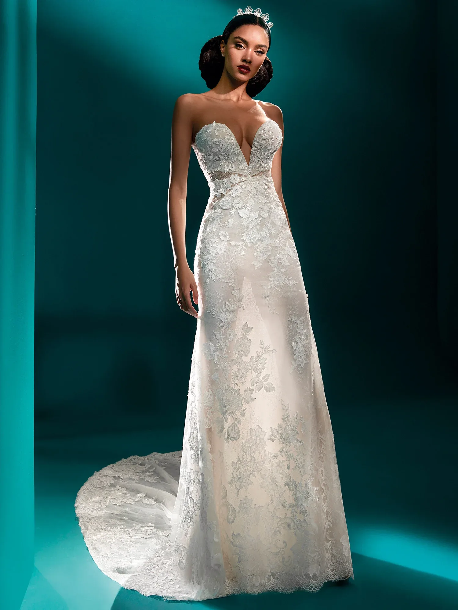 Vorderansicht eines trägerlosen Brautkleides mit tiefem Herzausschnitt und floralen Spitzenapplikationen. Der enge Schnitt betont die Figur, während die Schleppe aus zarter Spitze für einen eleganten Abschluss sorgt.