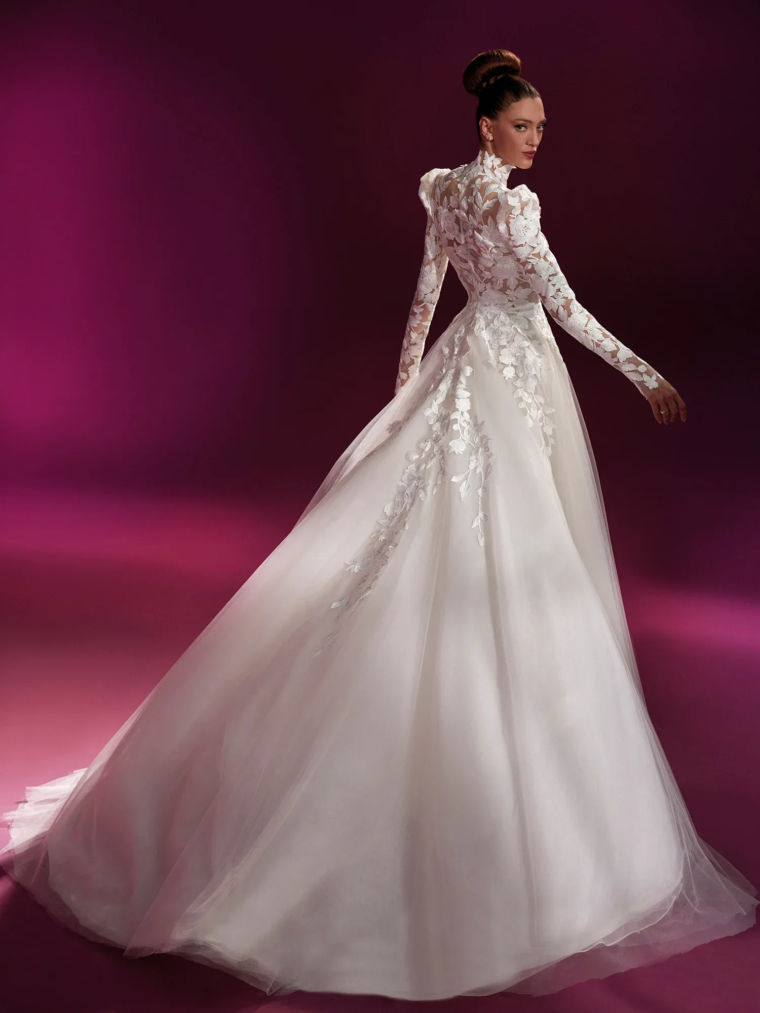 Rückenansicht eines Brautkleides mit langen Ärmeln und floralen Spitzenapplikationen. Das Kleid hat einen voluminösen Tüllrock, der sich zu einem eleganten Schleier ausbreitet und eine romantische Silhouette kreiert.