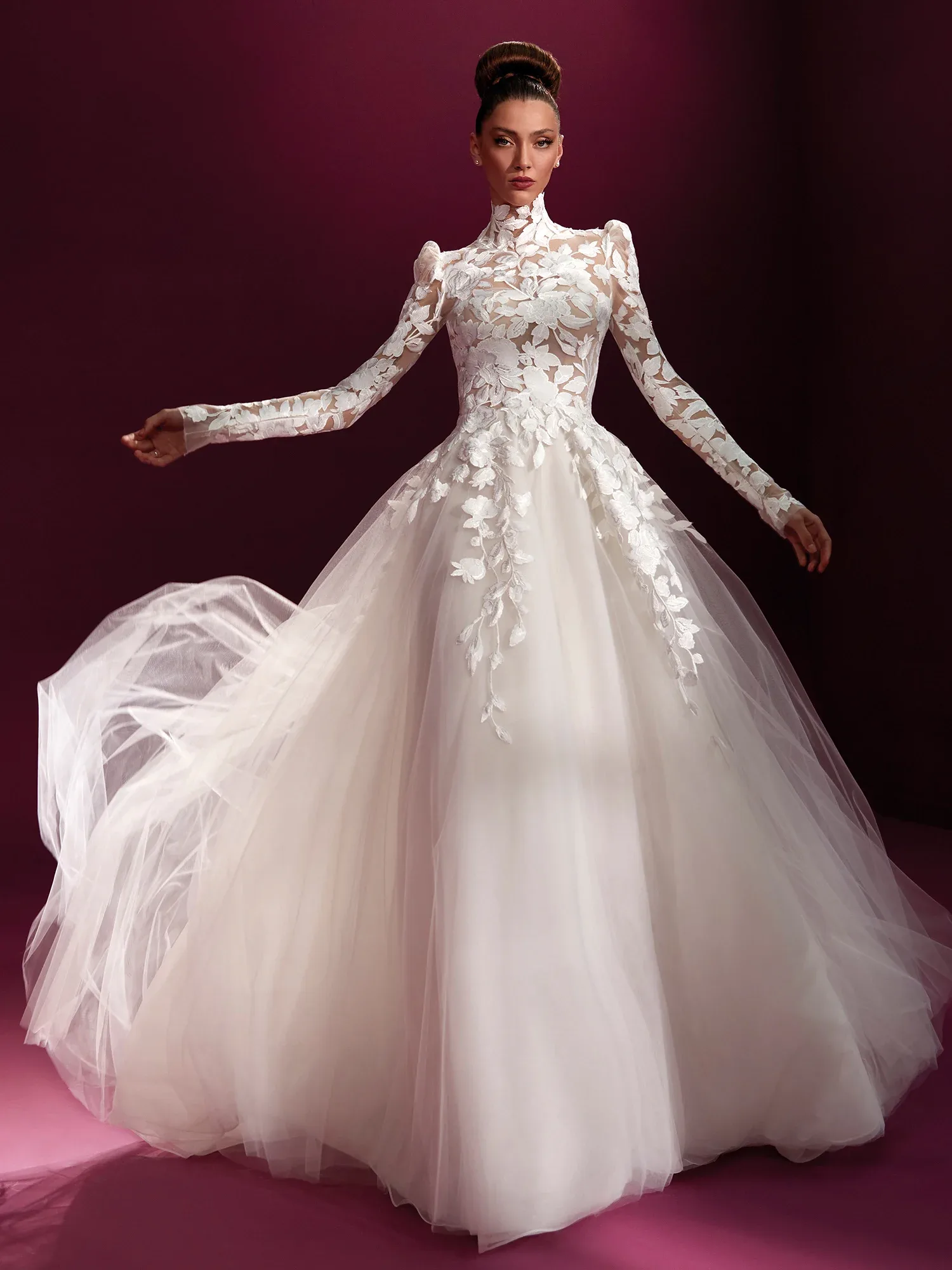 Vorderansicht eines Brautkleides mit hochgeschlossenem, transparentem Oberteil und floraler Spitze. Die langen Ärmel und der voluminöse Tüllrock sorgen für einen dramatischen und eleganten Look.