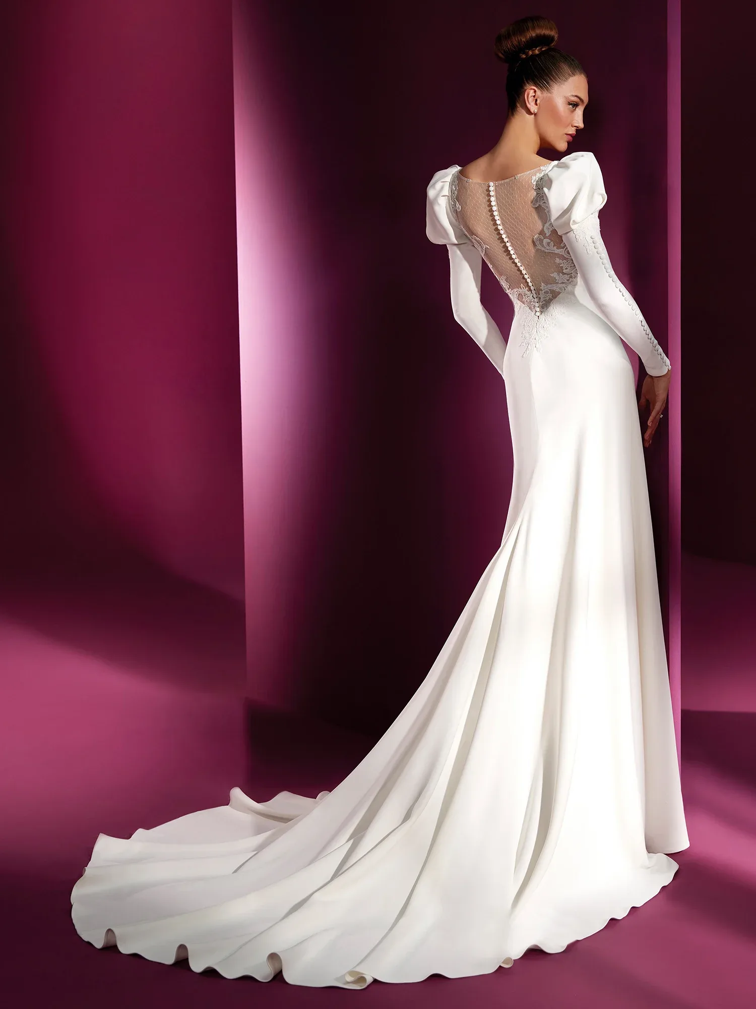 Elegantes Brautkleid mit langem Schleier, Rückansicht. Das Kleid hat lange Ärmel und einen transparenten Spitzeneinsatz am Rücken, der mit Knöpfen verziert ist. Der fließende Rock erstreckt sich zu einem sanften Zug.
