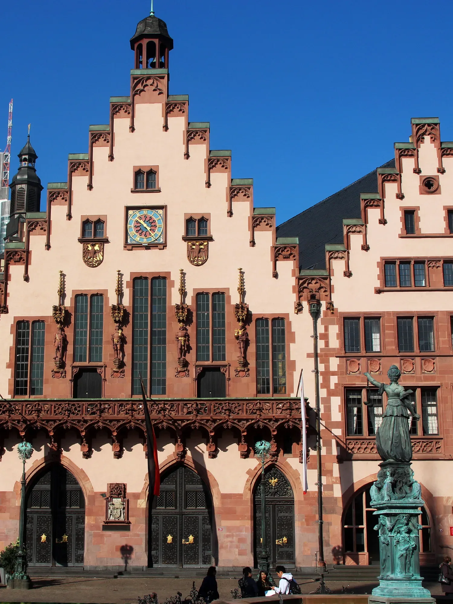Die Fassade des historischen Rathauses Römer in Frankfurt am Main, geprägt durch die charakteristischen Treppengiebel und rote Steinverzierungen, mit einer Uhr und Wappen, die an die reiche Geschichte des Gebäudes erinnern.