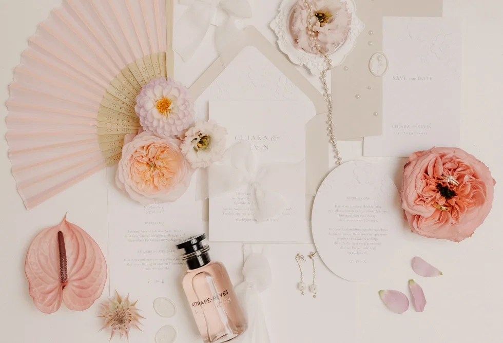 Stilvolle Flatlay-Komposition aus Hochzeits-Papeterie mit Einladungskarten, Save-the-Date, Blüten, Parfum und Schmuck in sanften Pastelltönen.
