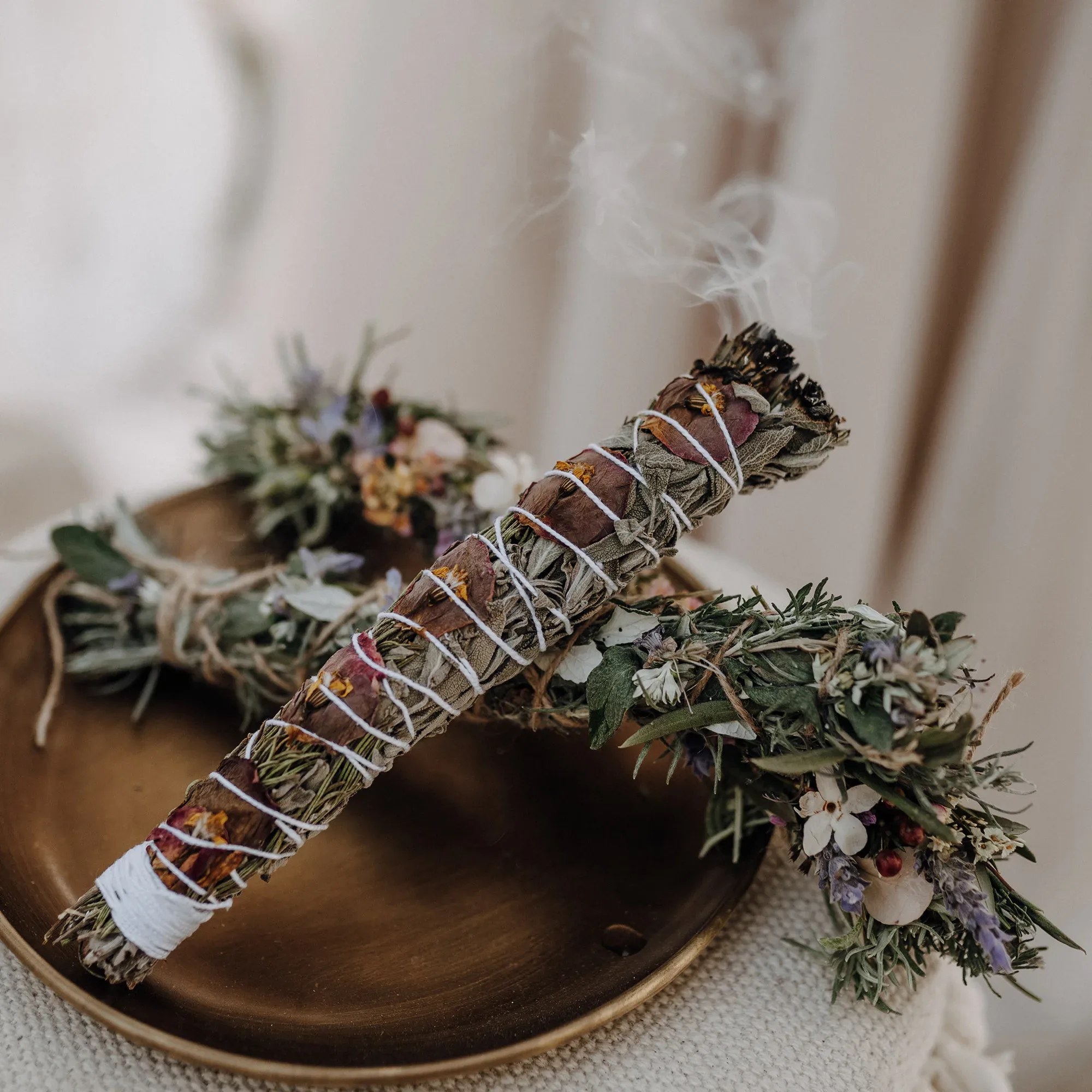 Räucherbündel aus getrockneten Kräutern und Blumen auf einem goldenen Tablett, leicht rauchend, für eine spirituelle Hochzeitszeremonie.