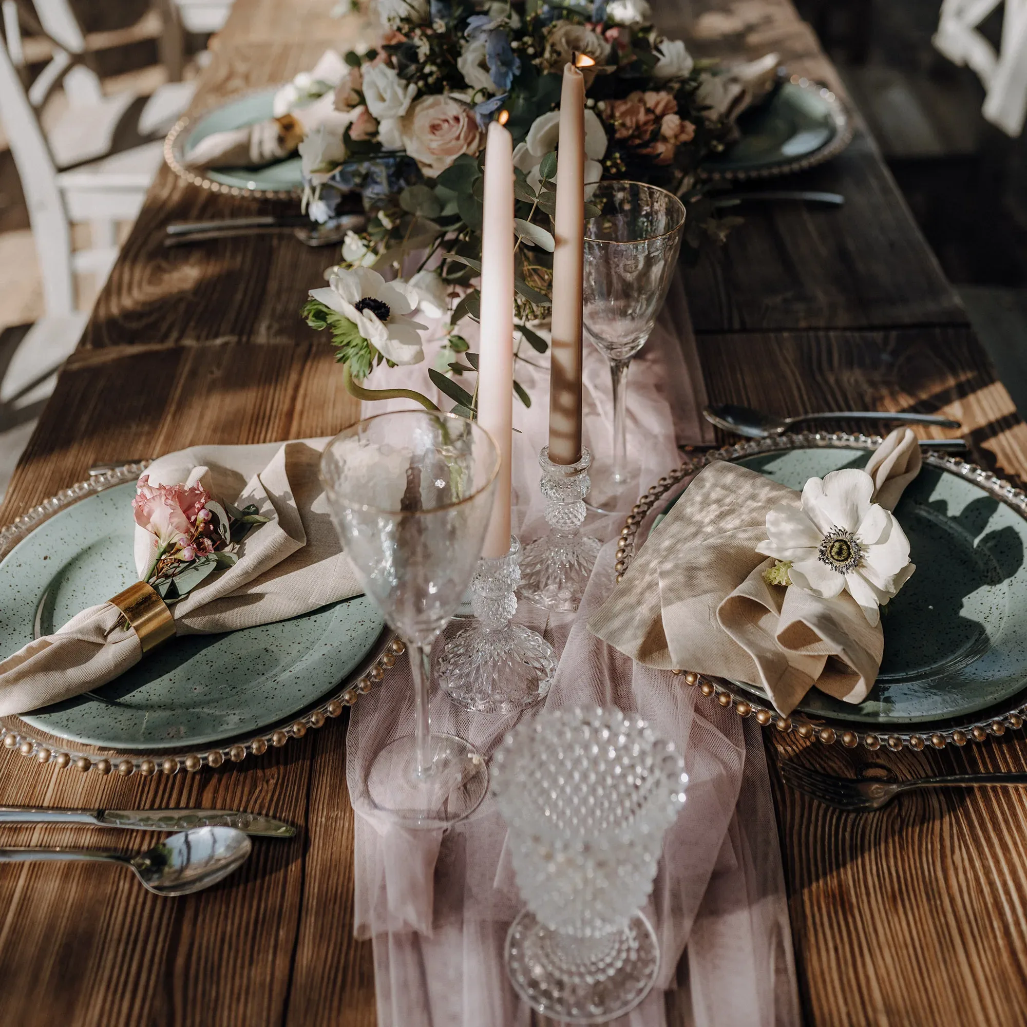 Elegant gedeckter Hochzeitstisch mit grünen Tellern, pastellfarbenen Blumen und Kerzen, verziert mit zarten Kristallgläsern und Servietten.