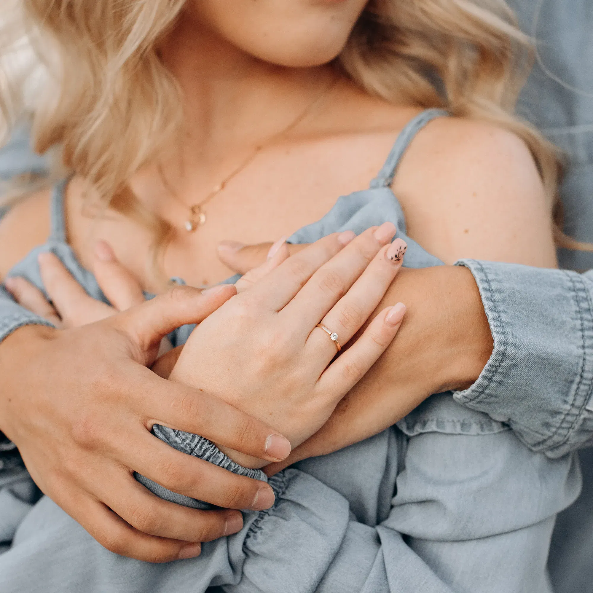 Nahaufnahme eines Paares, bei dem die Frau zärtlich die Hände ihres Partners auf ihrer Schulter hält, während sie ihren Verlobungsring zeigt.