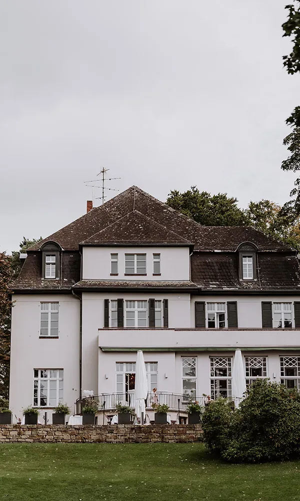 Ein elegantes weißes Herrenhaus mit grünen Fensterläden und einer Terrasse im Vordergrund.