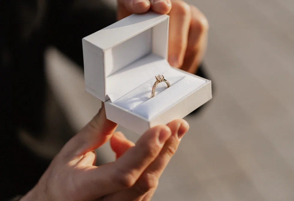 Geöffnete Ringschachtel mit funkelndem Verlobungsring in Nahaufnahme, gehalten in den Händen des Antragstellers