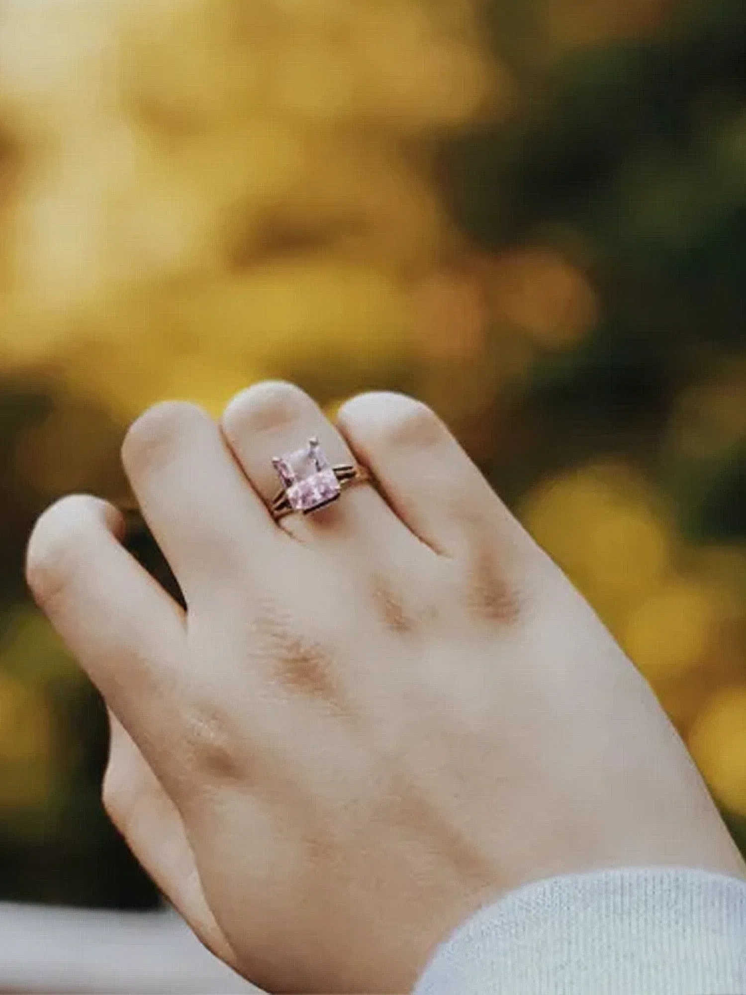 Eine Hand, die einen funkelnden, farbigen Verlobungsring in einem goldenen Licht zeigt, umgeben von herbstlichen Farben.