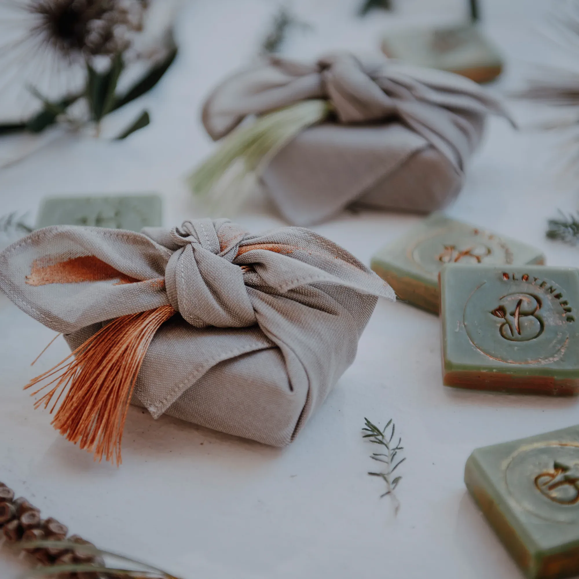Gastgeschenke in umweltfreundlicher Verpackung, verziert mit Stoff und Kräutern, daneben handgefertigte Seifen mit einem floralen Design.
