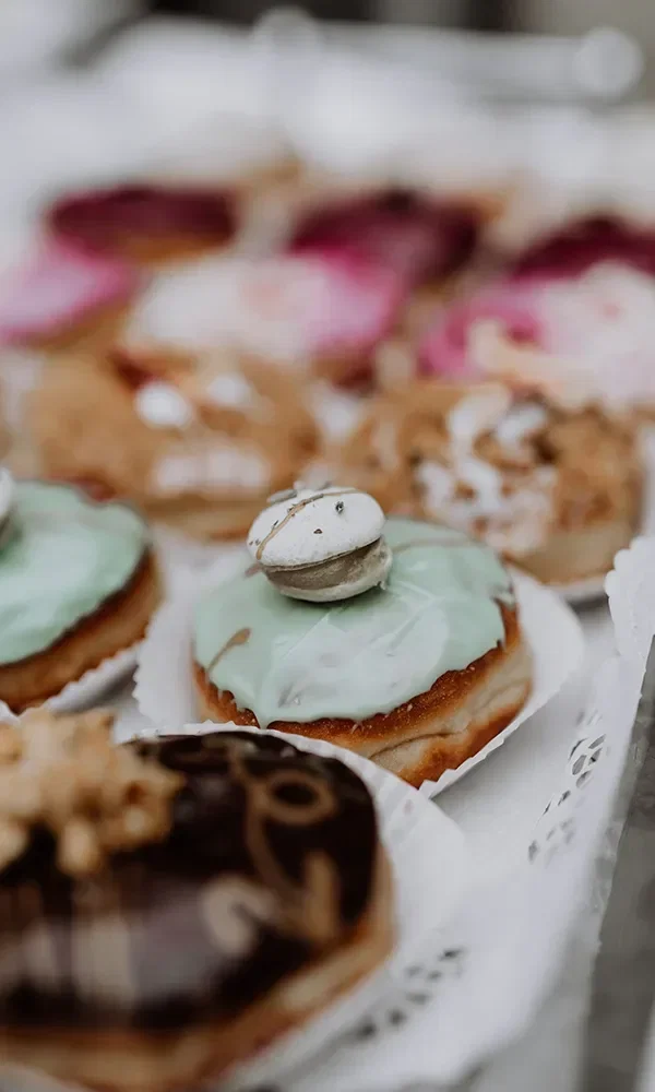 Ein Tablett mit verschiedenen Donuts, verziert mit buntem Zuckerguss und einer weißen Makrone auf einem Donut mit hellgrünem Guss.