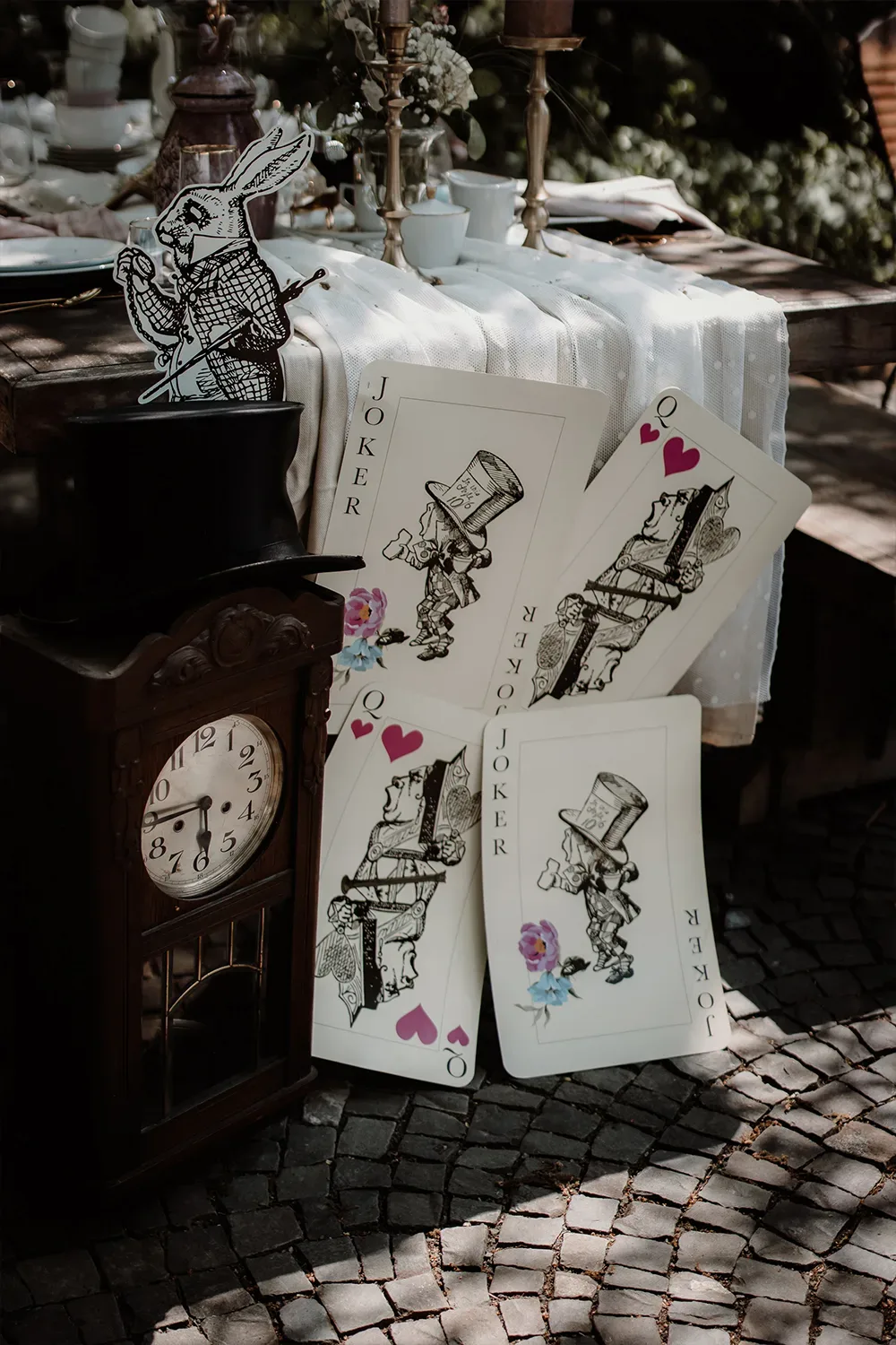 Eine verspielte Hochzeitsdeko im Alice im Wunderland-Stil mit übergroßen Spielkarten, einer antiken Uhr und einem Hasen aus der Geschichte.