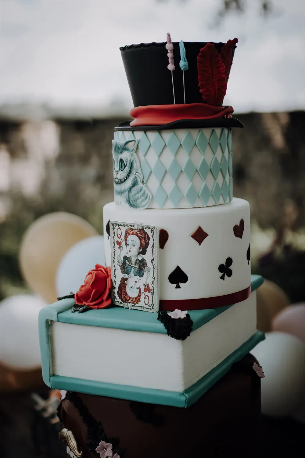 Eine mehrstöckige Hochzeitstorte im "Alice im Wunderland"-Thema mit Spielkartenmotiven, einem Hut und einem Buch als Basis.