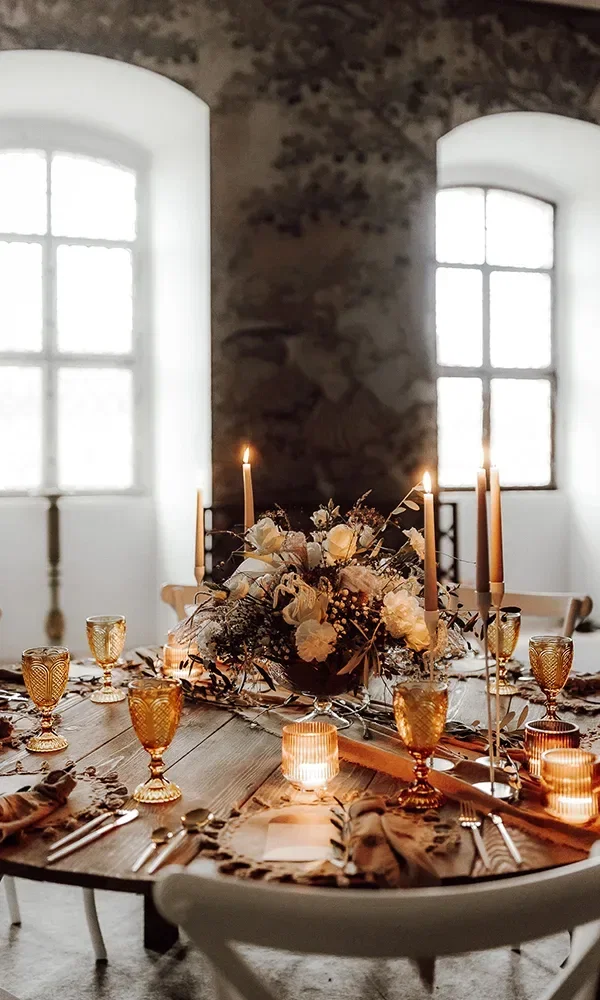 Ein wunderschön gedeckter Hochzeitstisch mit goldenen Gläsern, Kerzen und floralen Arrangements in einem rustikalen Saal.