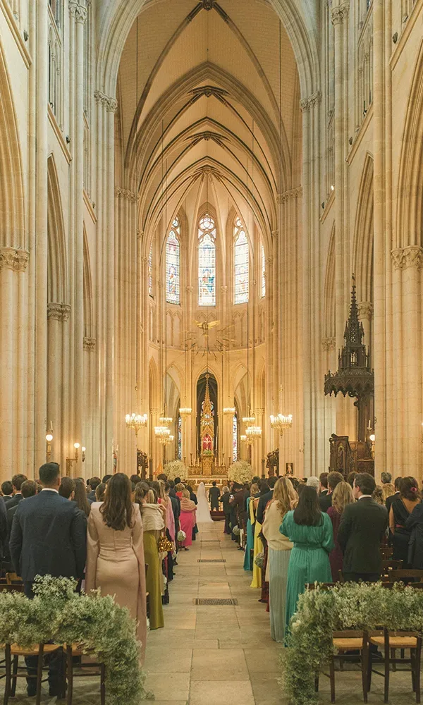 Ein beeindruckender Blick auf den Innenraum einer großen gotischen Kirche während einer Hochzeitszeremonie. Die Gäste sitzen auf den Holzbänken, während das Brautpaar vor dem festlich geschmückten Altar steht.