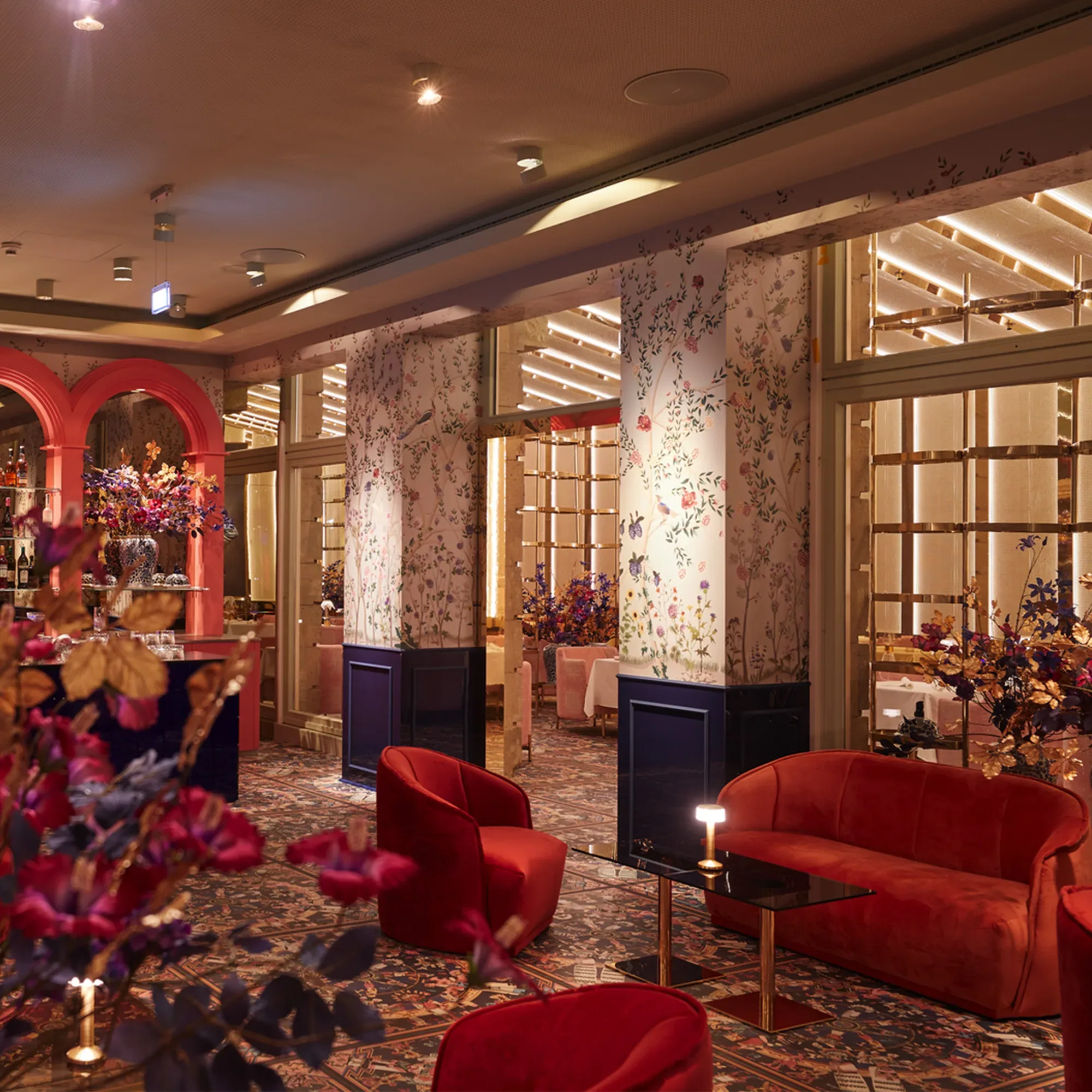 Eine luxuriöse Lounge mit roten Sofas und eleganten Blumendekorationen. Die Wände sind mit floralen Mustern verziert, und die moderne Beleuchtung unterstreicht die einladende, edle Atmosphäre.