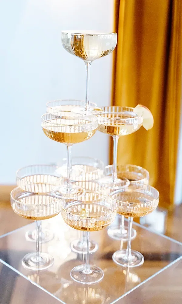Ein eleganter Champagner-Turm aus geschichteten Gläsern, in die Champagner gefüllt ist. Die Gläser reflektieren das Licht, und ein Glas am Rand ist mit einer Zitronenscheibe verziert.