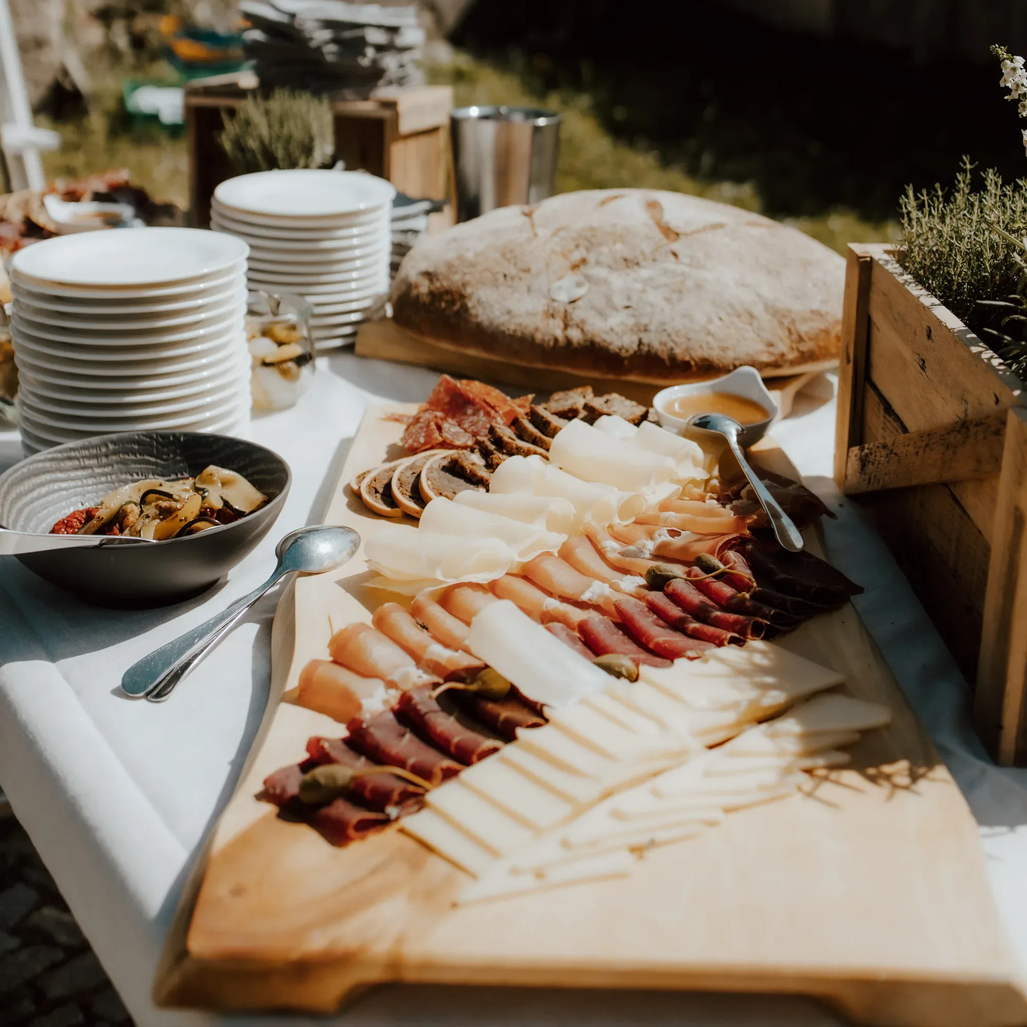 Ein rustikales Hochzeitsbuffet mit einer Auswahl an verschiedenen Käsesorten und Wurstspezialitäten, angerichtet auf einem Holzbrett, begleitet von Brot und Beilagen.