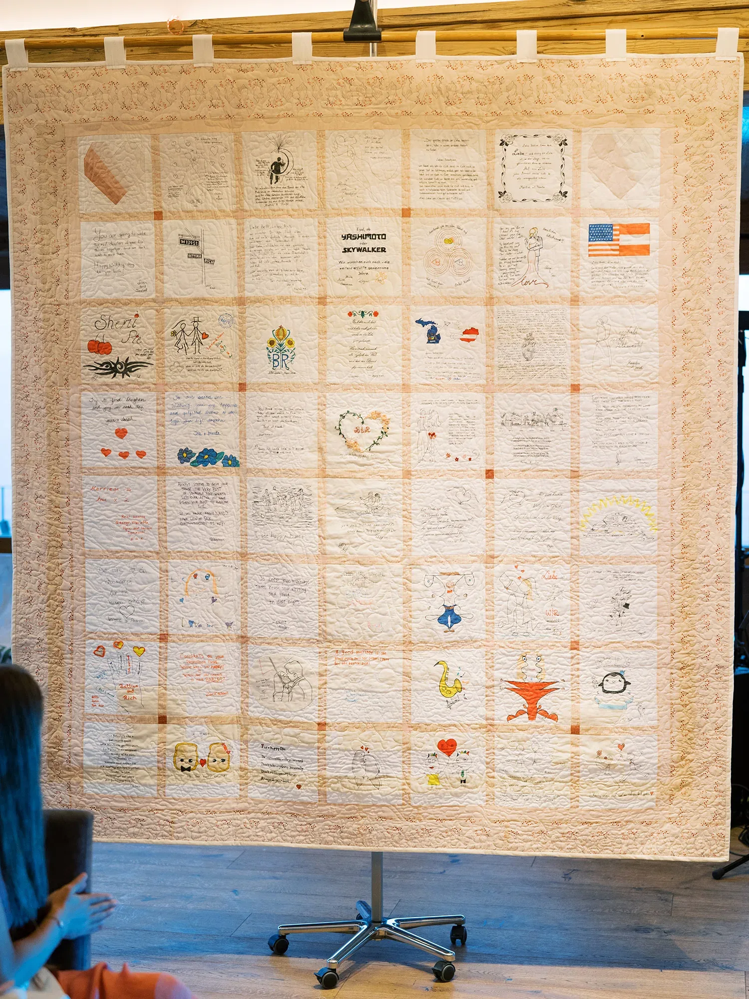 Handgemachter Quilt mit individuellen Nachrichten und Zeichnungen von Hochzeitsgästen, sorgfältig auf quadratischen Stofffeldern arrangiert.