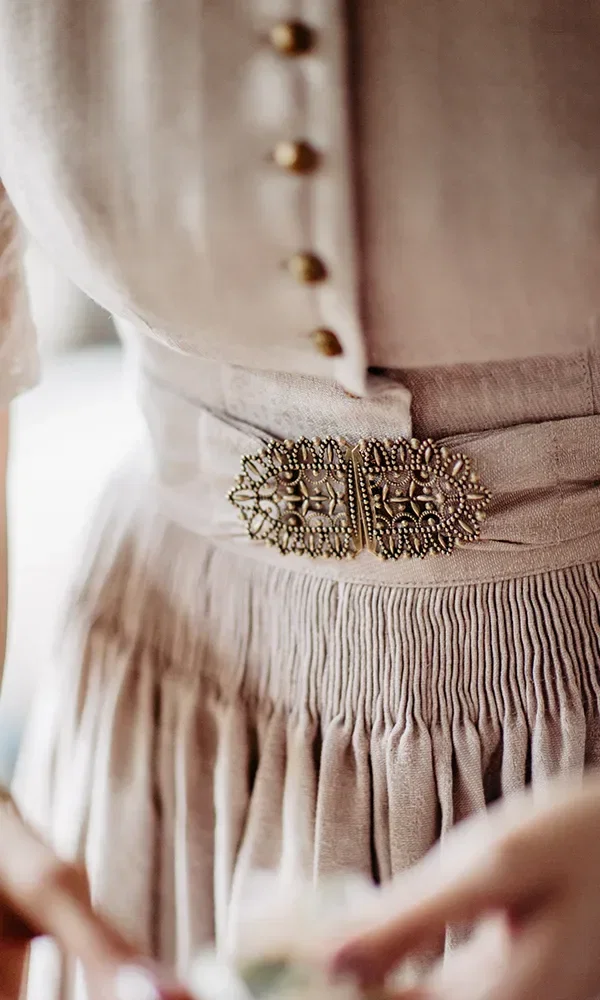 Nahaufnahme eines traditionellen Hochzeitskleids, einem Dirndl, mit feinen Knöpfen und einer kunstvollen, goldenen Schnalle an der Taille.