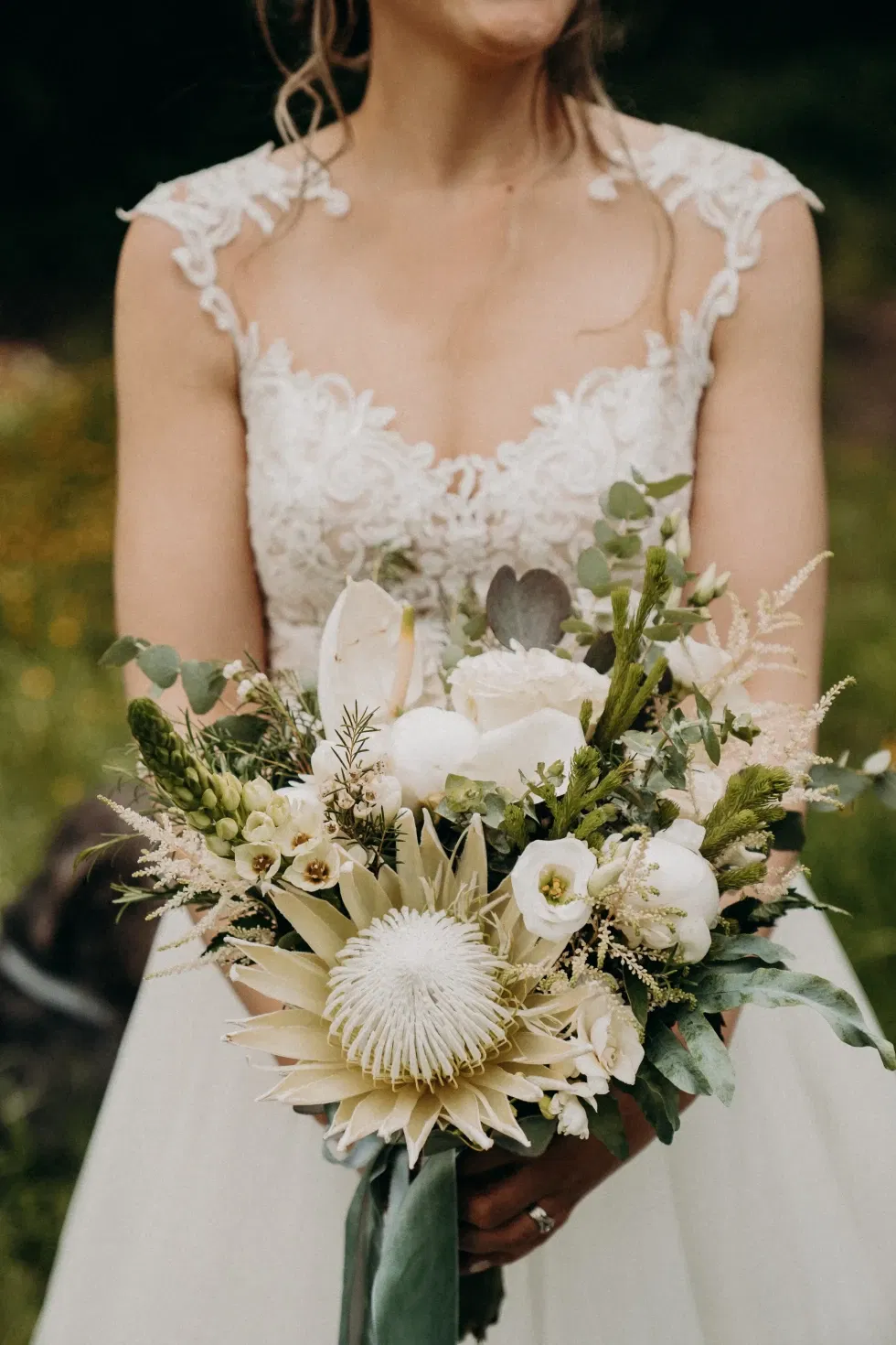 Braut hält ihren Brautstrauße aus weißen Blumen und grünen Zweigen in die Kamera.