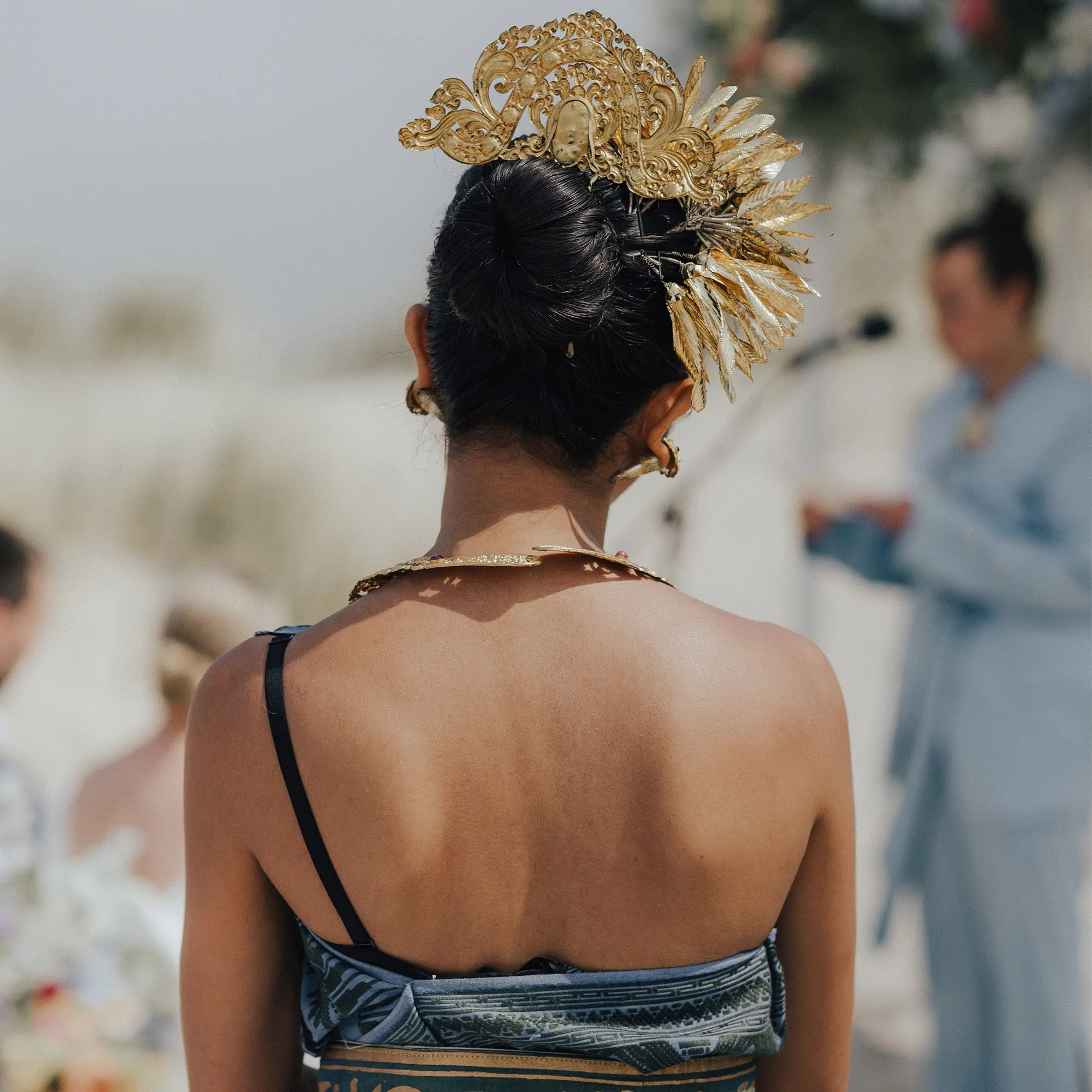Frau im traditionellen balinesischen Hochzeitsgewand mit goldenen Kopfschmuck steht mit dem Rücken zur Kamera.
