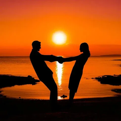 Die Silhoutten eines sich an den Händen haltenden Paares vor einem Sandstrand mit Sonnenuntergang.