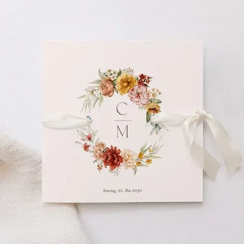 Eine Hochzeitseinladung mit einer zarten rosafarbenen Basis, verziert mit einem Blumenbouquet in den Farben Creme, Gelb und Rot mit den Initialen "C M". Ein cremefarbenes Band ziert die linke Seite, und das Datum Samstag, 22. Mai 2030, ist unten angegeben.
