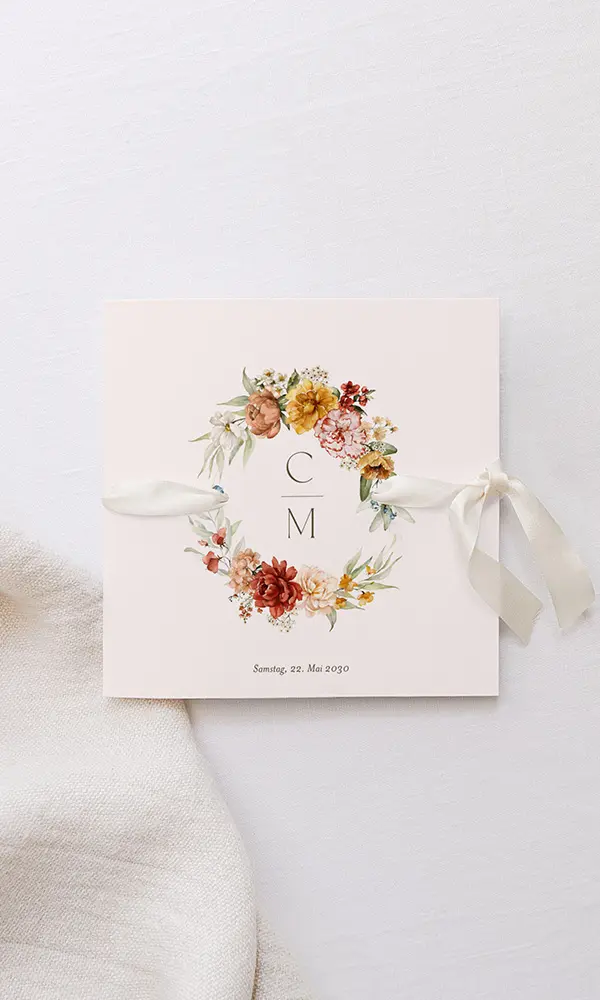 Eine Hochzeitseinladung mit einer zarten rosafarbenen Basis, verziert mit einem Blumenbouquet in den Farben Creme, Gelb und Rot mit den Initialen "C M". Ein cremefarbenes Band ziert die linke Seite, und das Datum Samstag, 22. Mai 2030, ist unten angegeben.